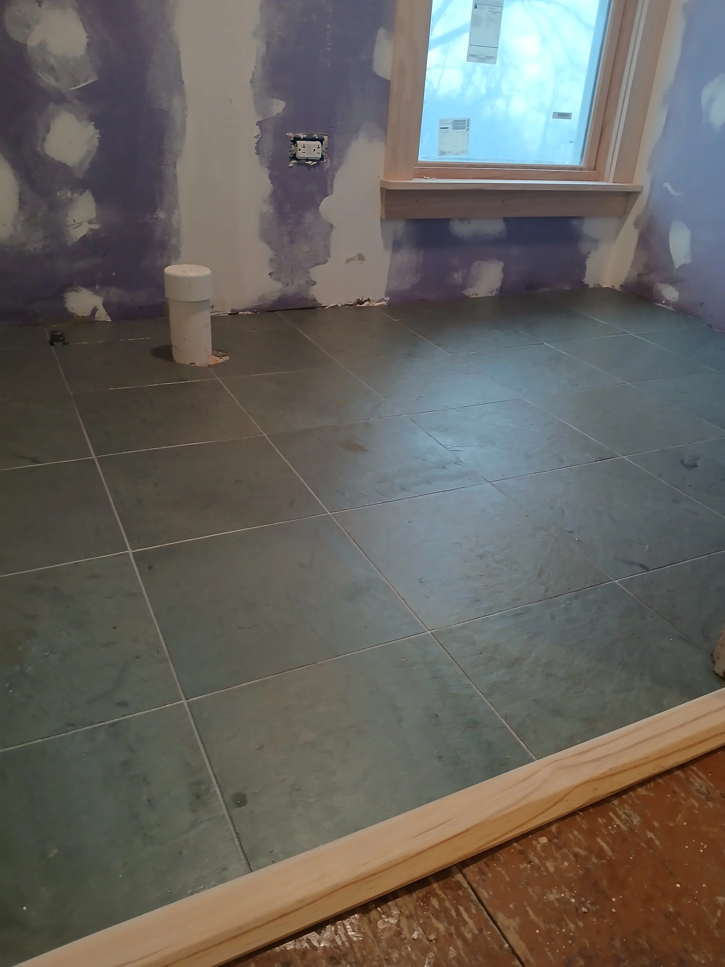 Room under construction with green tiles on the floor, a window, and unfinished purple walls