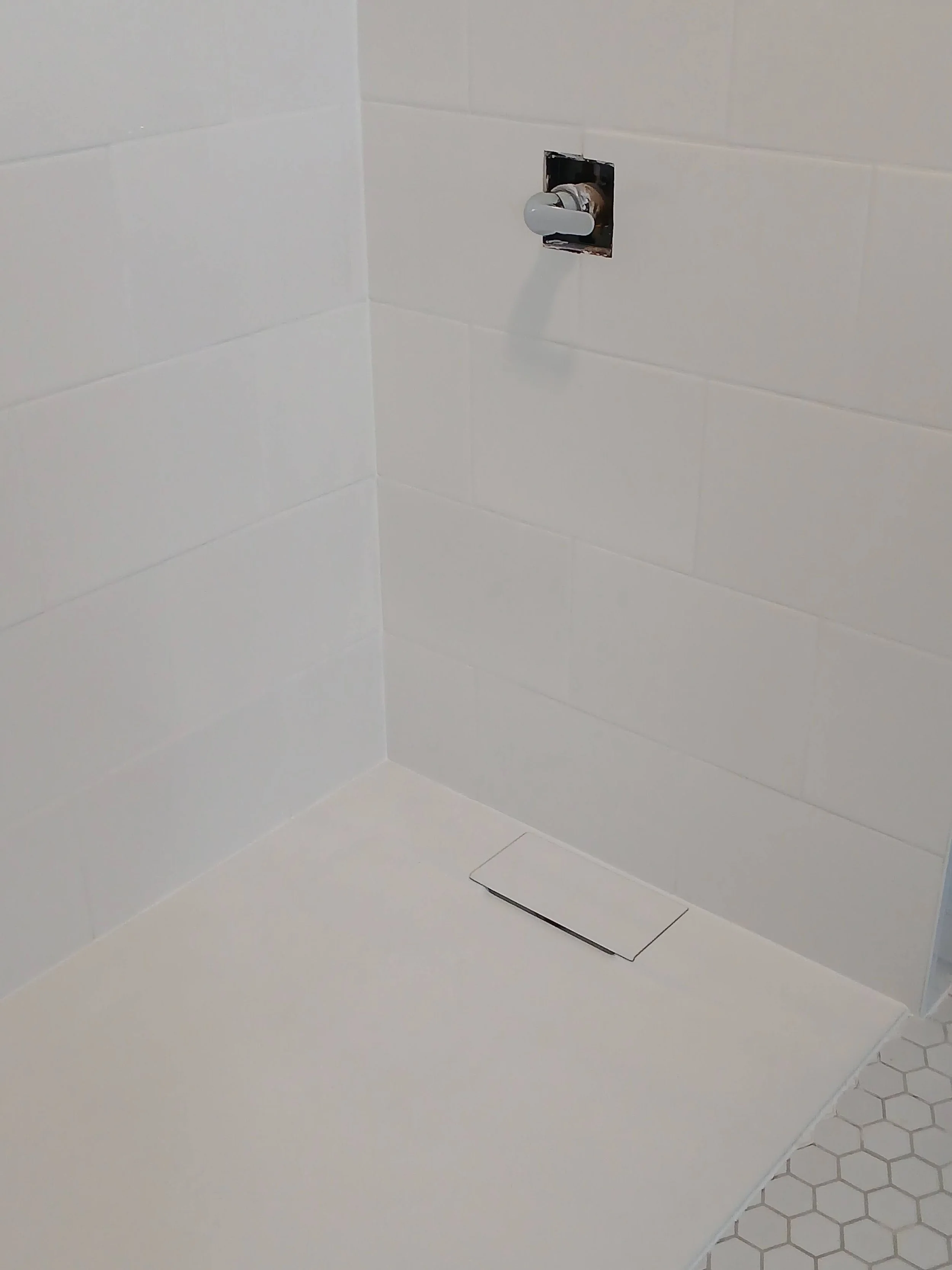 Clean shower area with white tiles, a drain in the floor, and a faucet handle protruding from the wall.