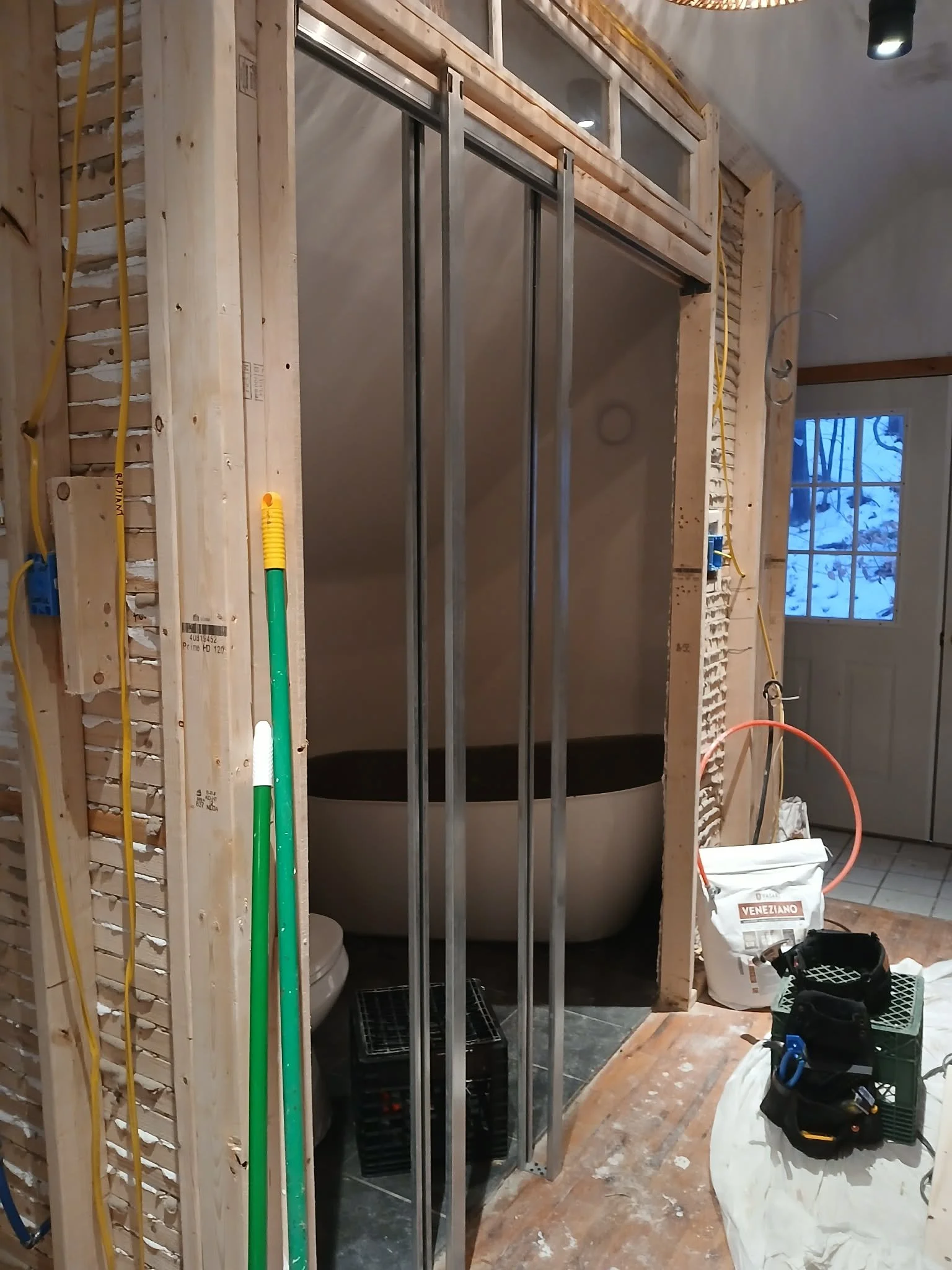 Bathroom under construction with metal framing, partially installed bathtub, and building tools and materials around.