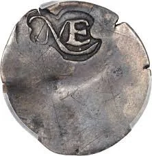 A round, metallic object with a stylized number 3 or letter E engraved on the top. It has a weathered surface with some scratches and spots.