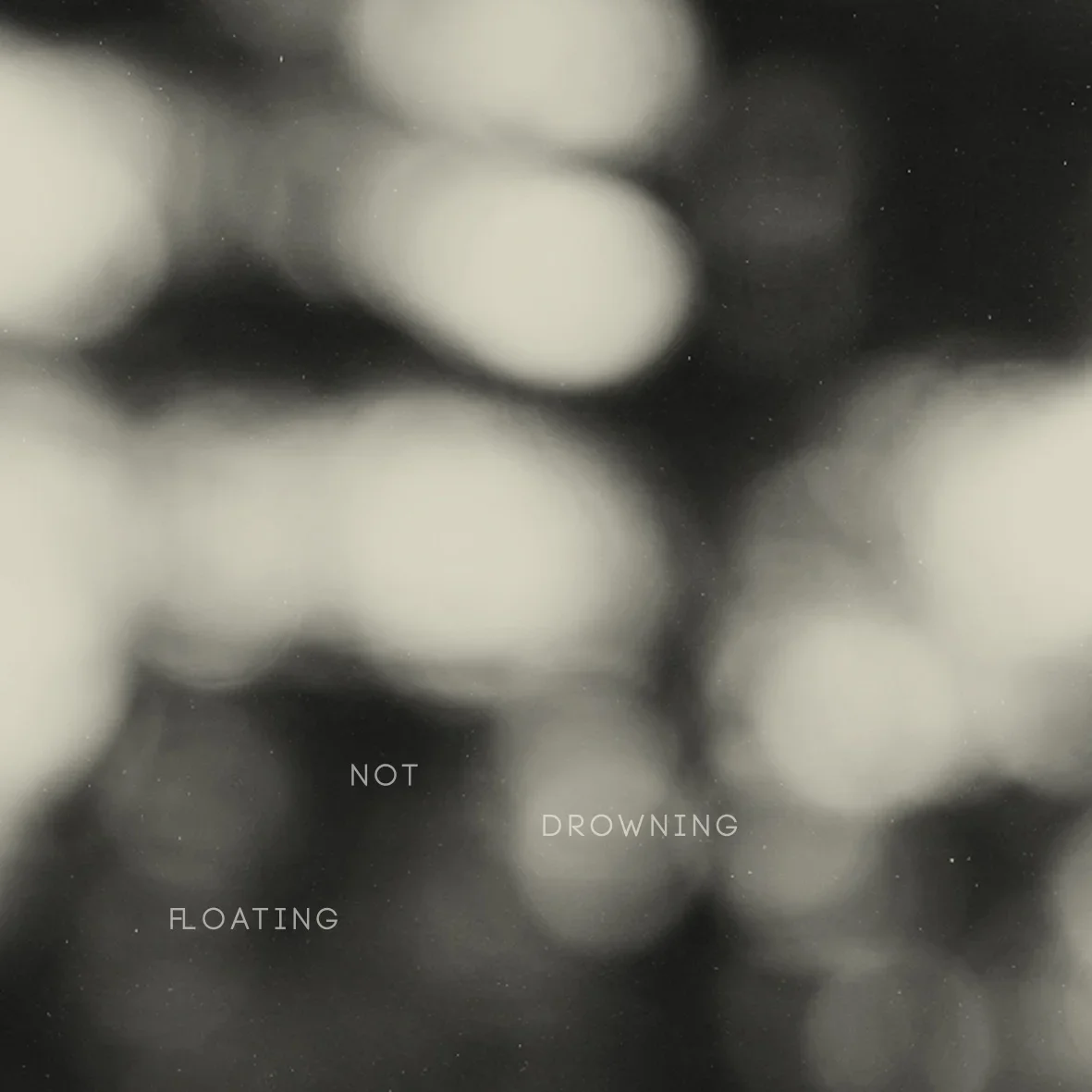 Black and white abstract image with blurred circular lights and the words 'NOT DROWNING, FLOATING' on it.