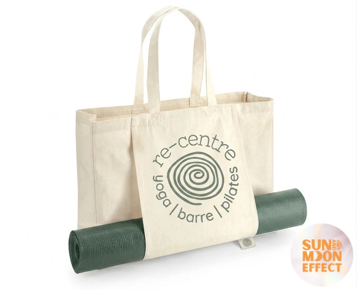 A reusable tote bag with a yoga mat and a smaller bag in front, labeled with words related to Pilates and barre exercise.