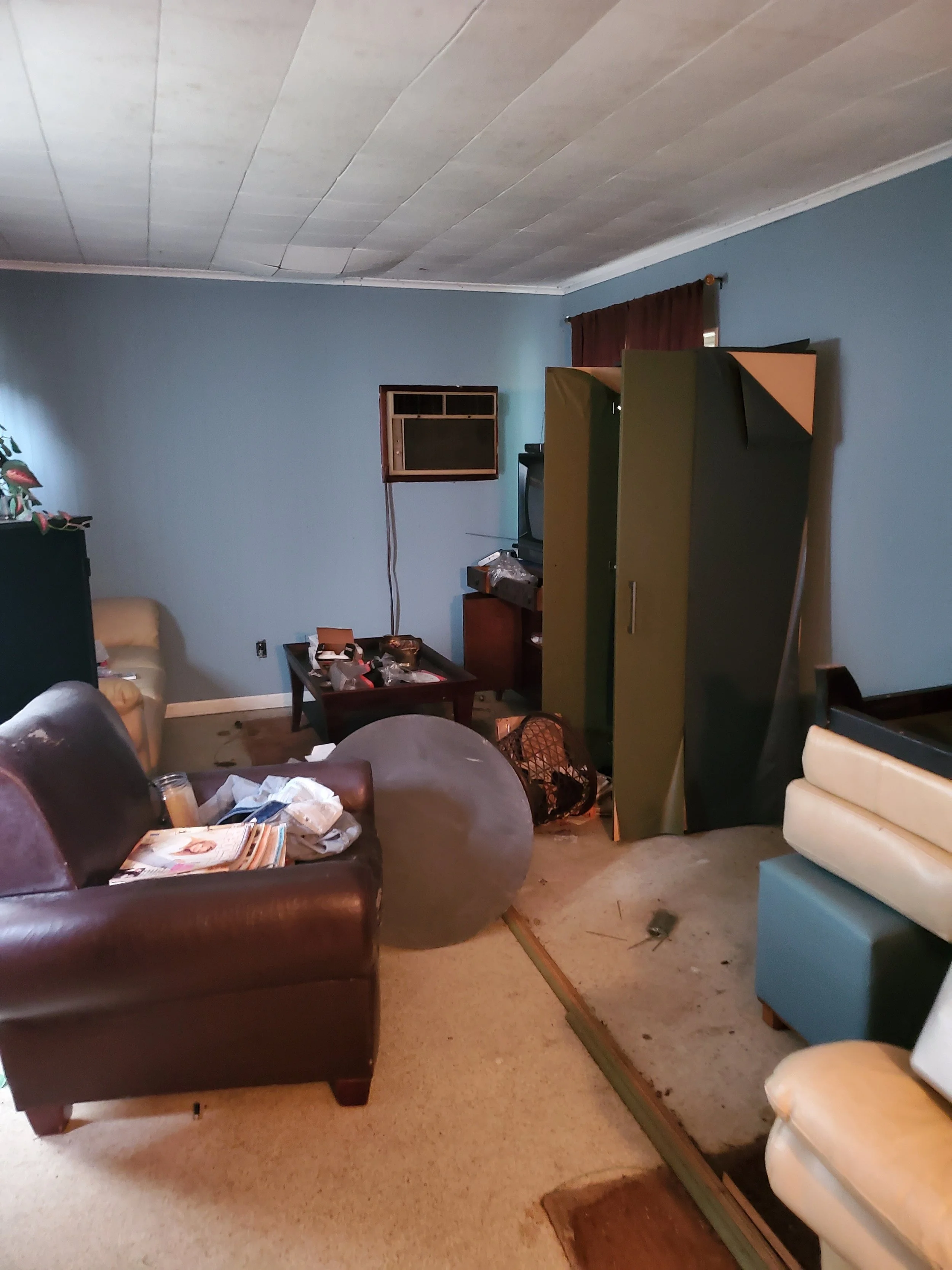 Disorganized living room with broken flooring, scattered items, and furniture.