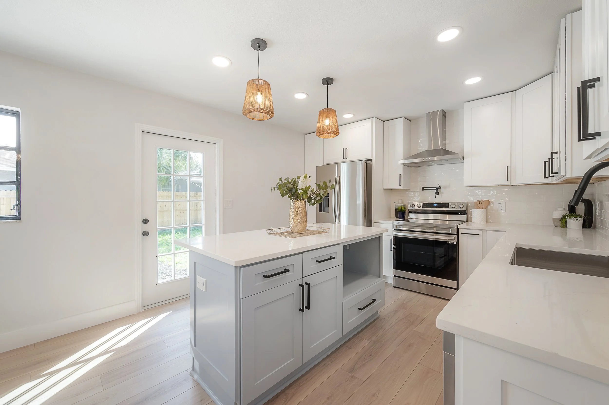 Modern white kitchen with a central island, stainless steel appliances, and pendant lighting fixtures.