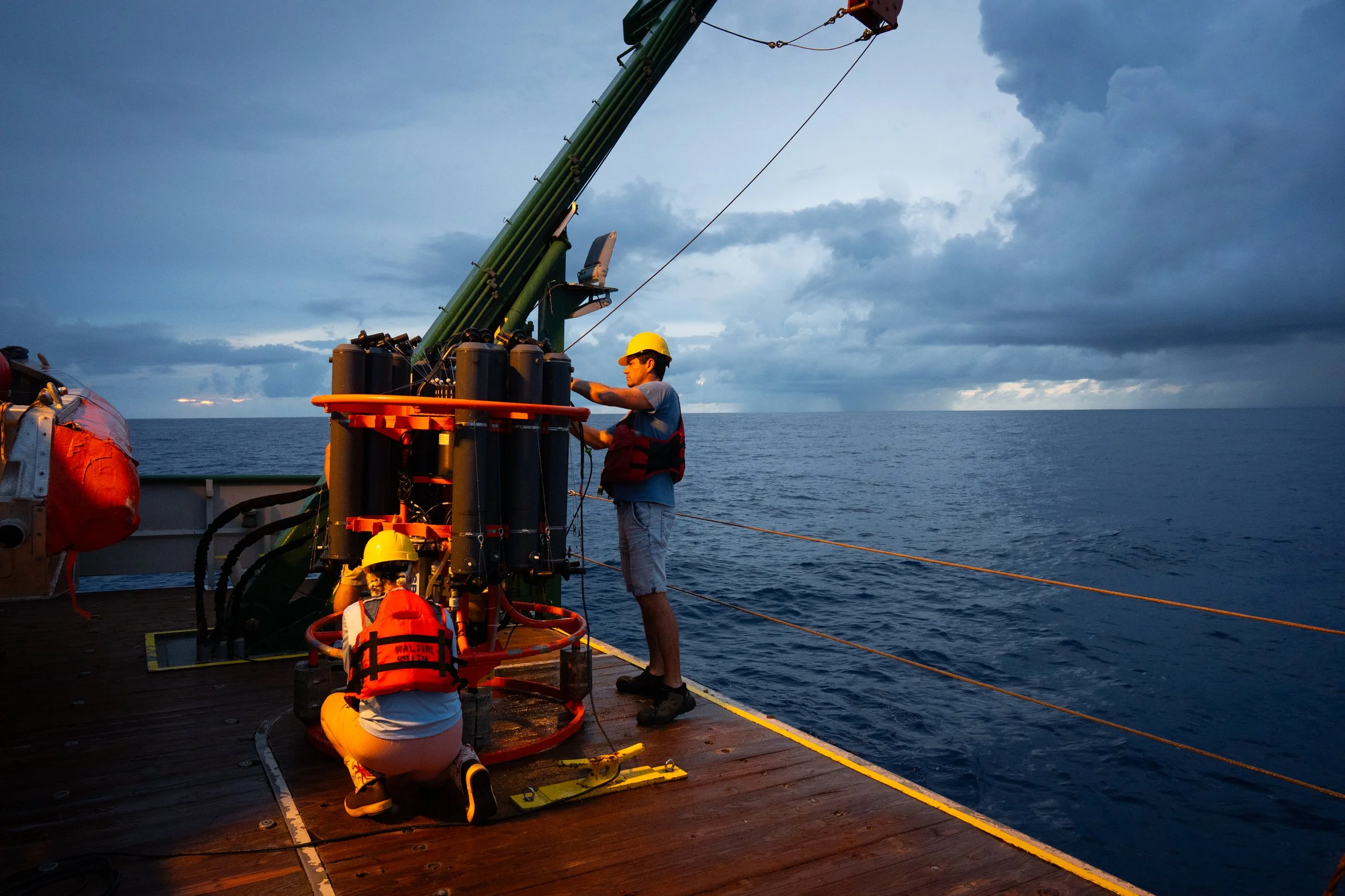 Tyler Christian and Denis Volkov, an oceanographer, collect ocean water from a recovered instrument during sampling operations.