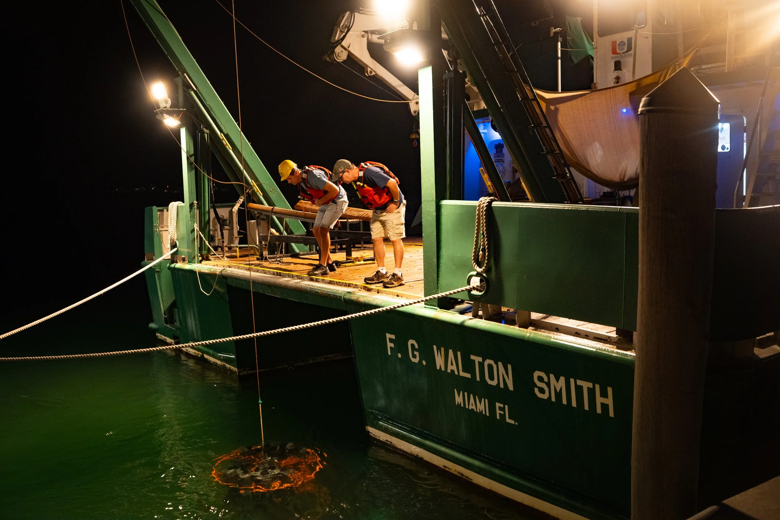 Oceanographers Denis Volkov, left, and Ryan H. Smith watch as an instrument used to sample the ocean is lowered into the water before the vessel departs for Bahamian waters.