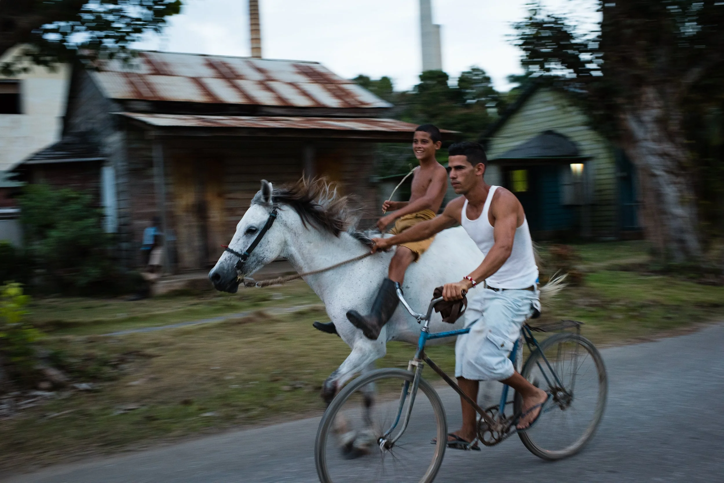 A boy rides a white horse as a bicyclist catches a ride alongside him in Camilo Cienfuegos, Cuba, March 27, 2015. Formerly known as Hershey, the sugar mill town east of Havana was built by American chocolatier Milton Hershey, who provided affordable 