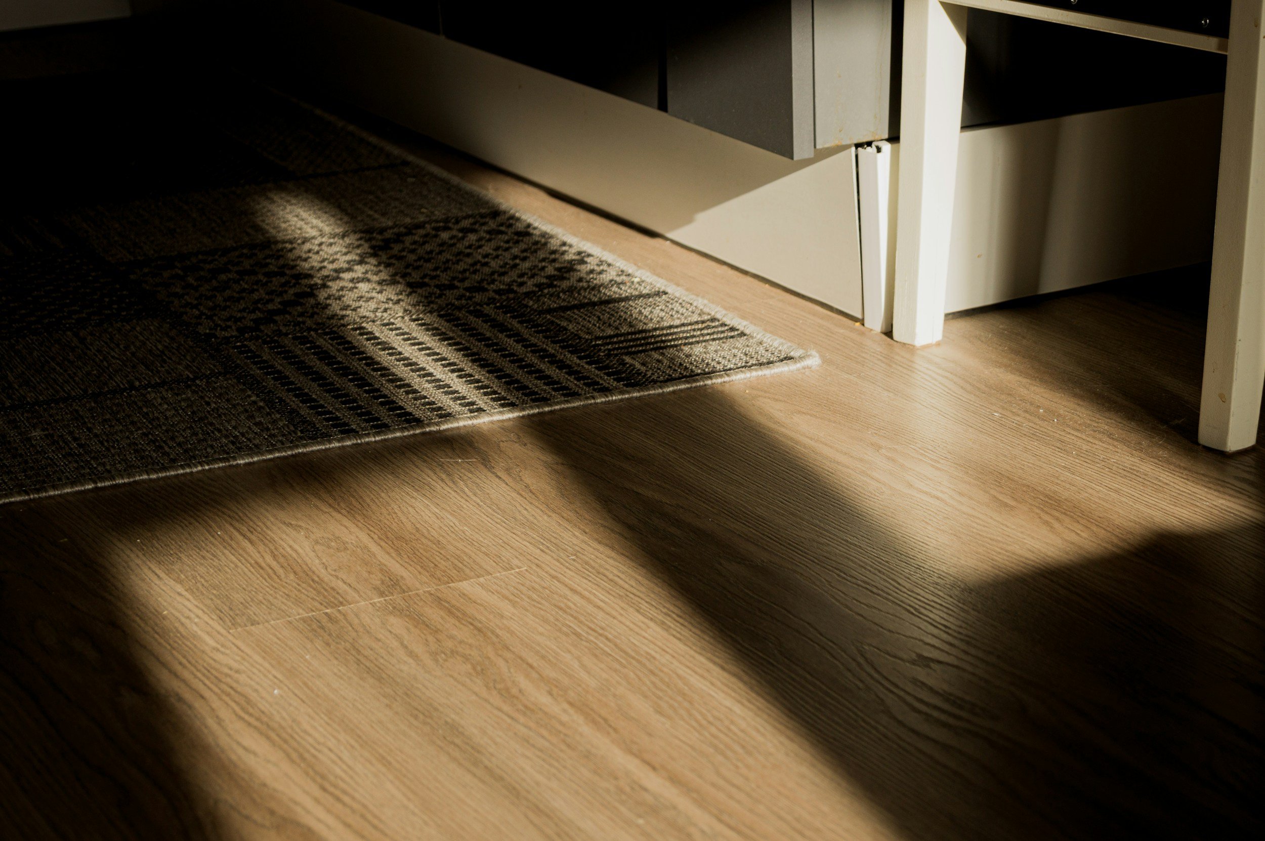 Sunlight shining on a patterned rug and a wooden floor next to a white cabinet.
