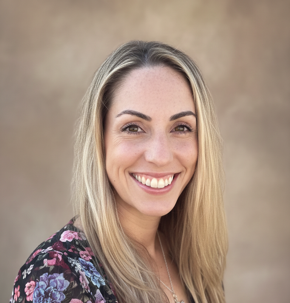 A woman with long blonde hair, wearing a floral top, smiling outdoors against a neutral background.