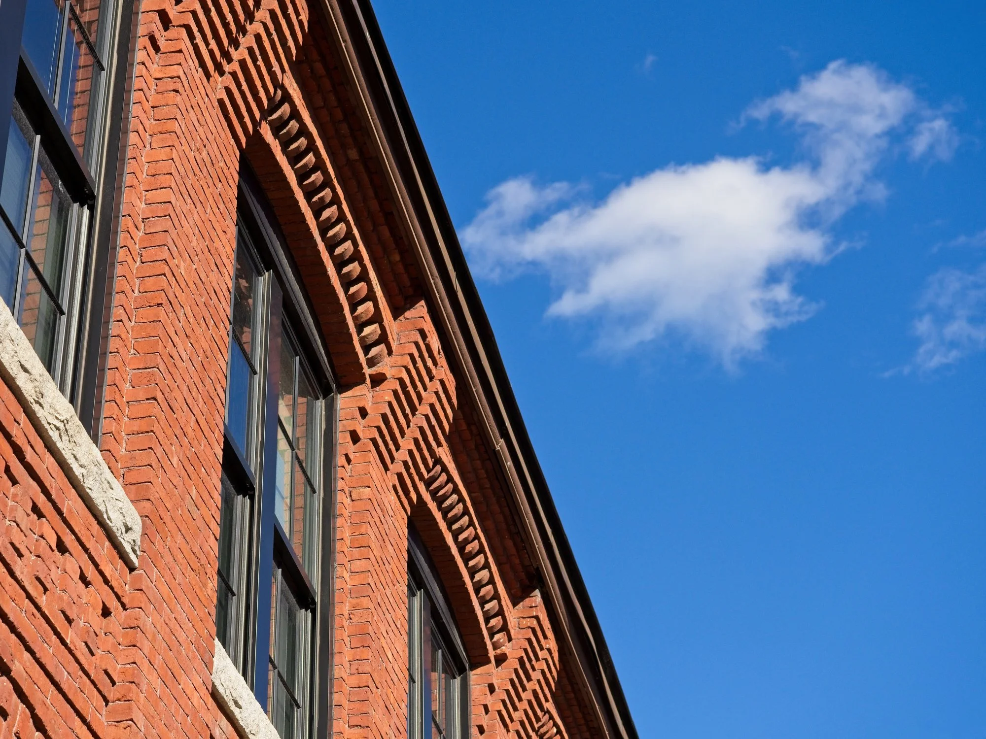 Close-up of a red brick building with rectangular windows under a clear blue sky with some white clouds.