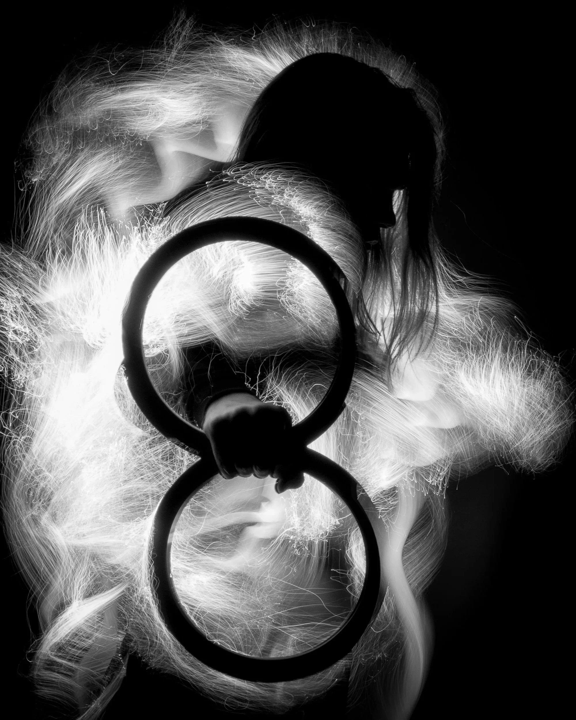 A person holding a flashlight in front of their face, creating bright light trails and a silhouette in a black and white photograph.