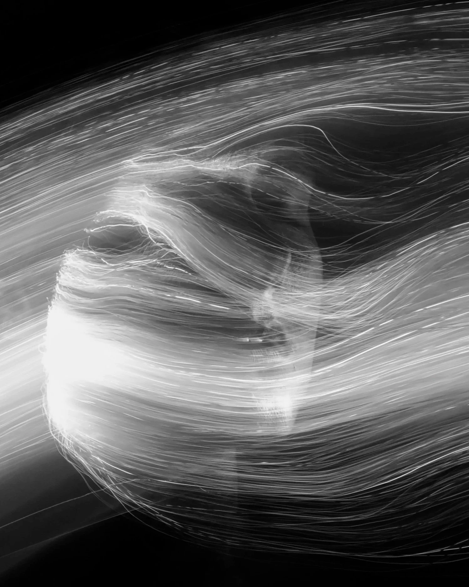 Abstract black-and-white photo of flowing light streaks forming a swirling pattern.