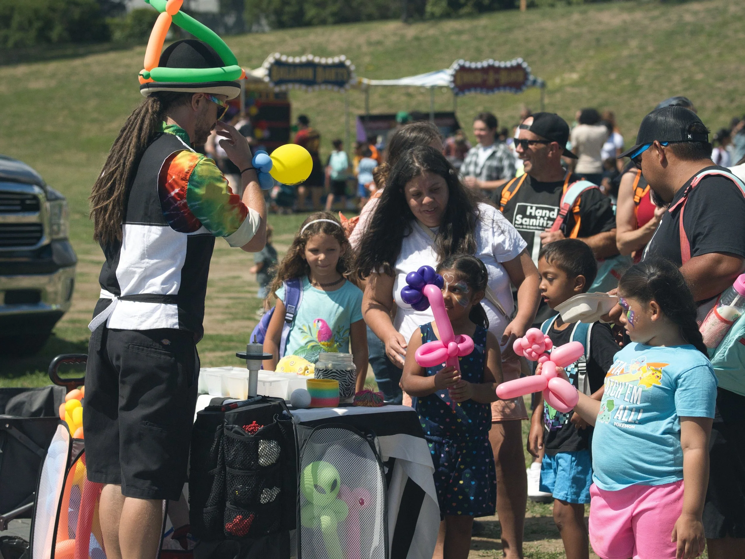 A balloon artist making balloon animals for children at an outdoor festival.