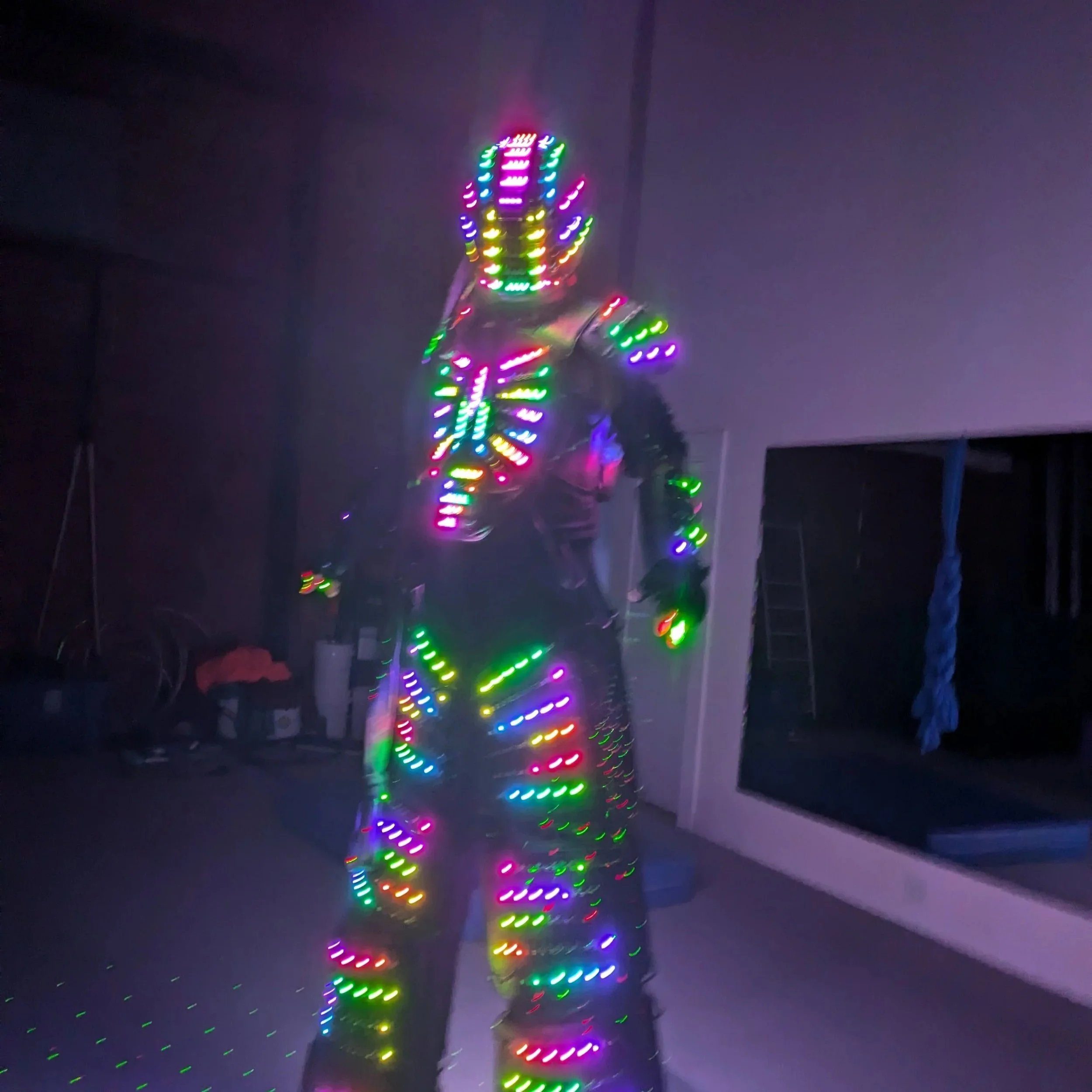Person dressed in an LED light-up costume with multicolored lights, standing indoors at night.