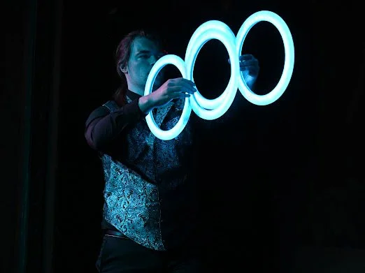 Person holding three interconnected neon rings in a dark setting.