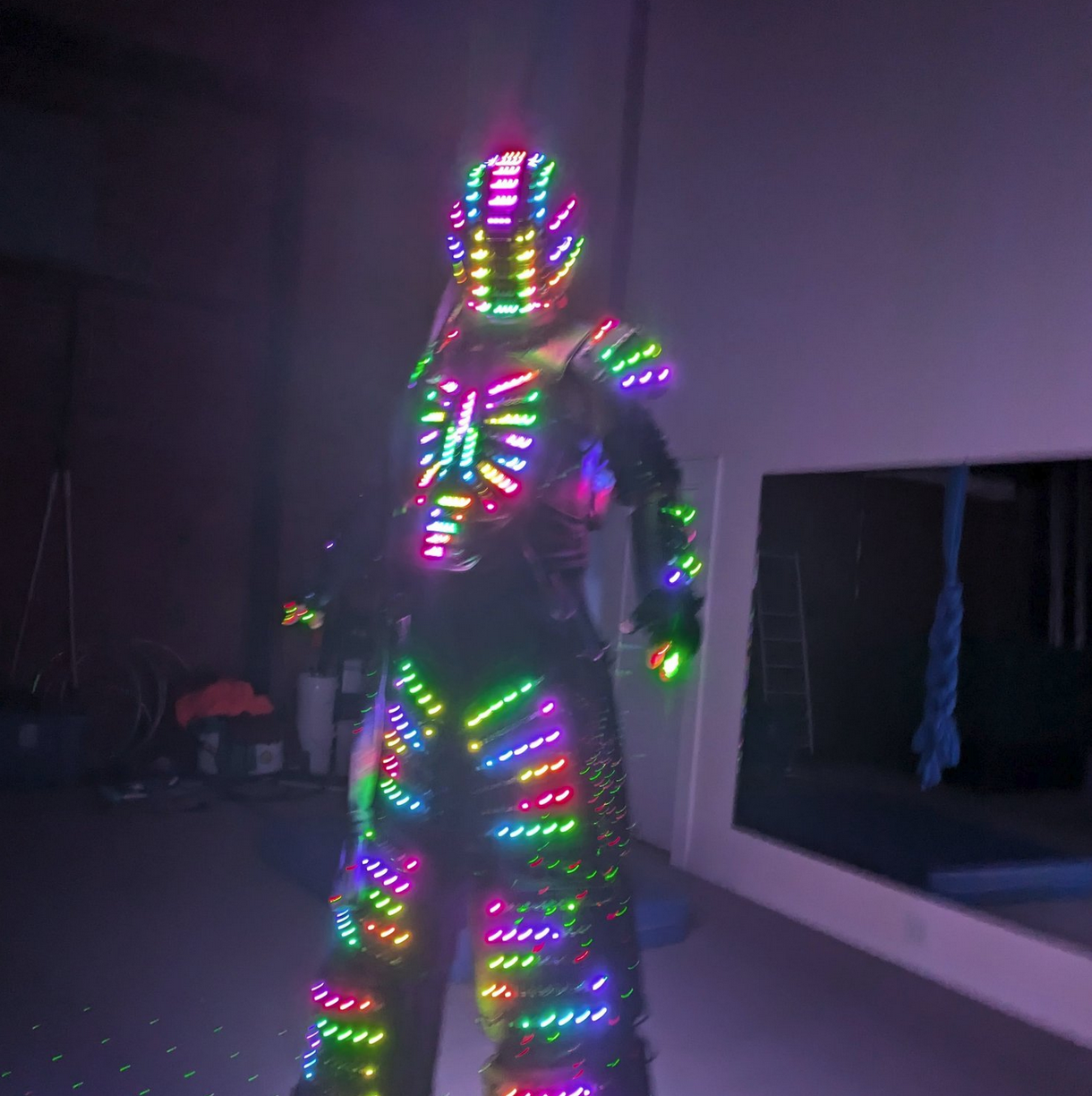 Person wearing a suit covered in multicolored LED lights in a dark room.