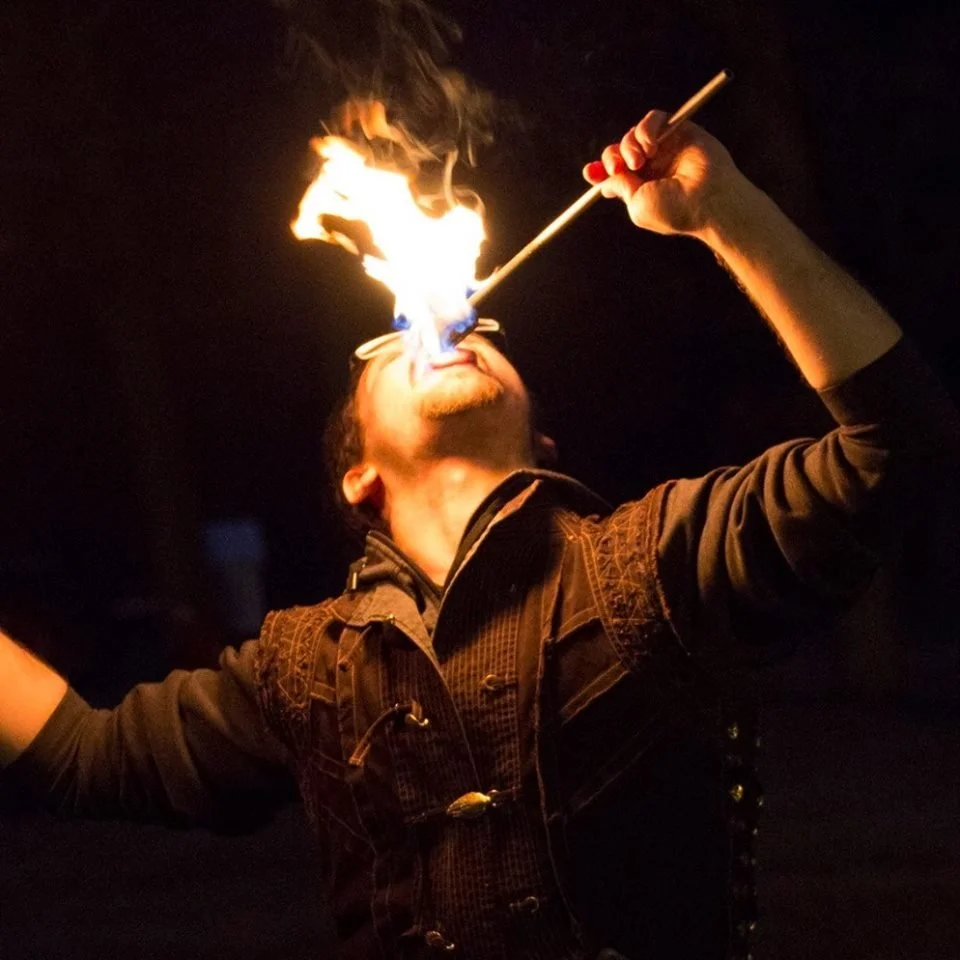 A person performing a fire-eating act, with flames coming out of their mouth at night.