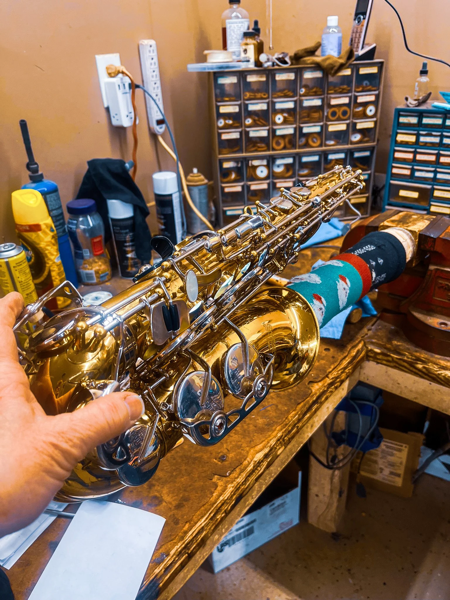 Close-up of a gold-colored alto saxophone being held over a woodworking workbench in a cluttered workshop.