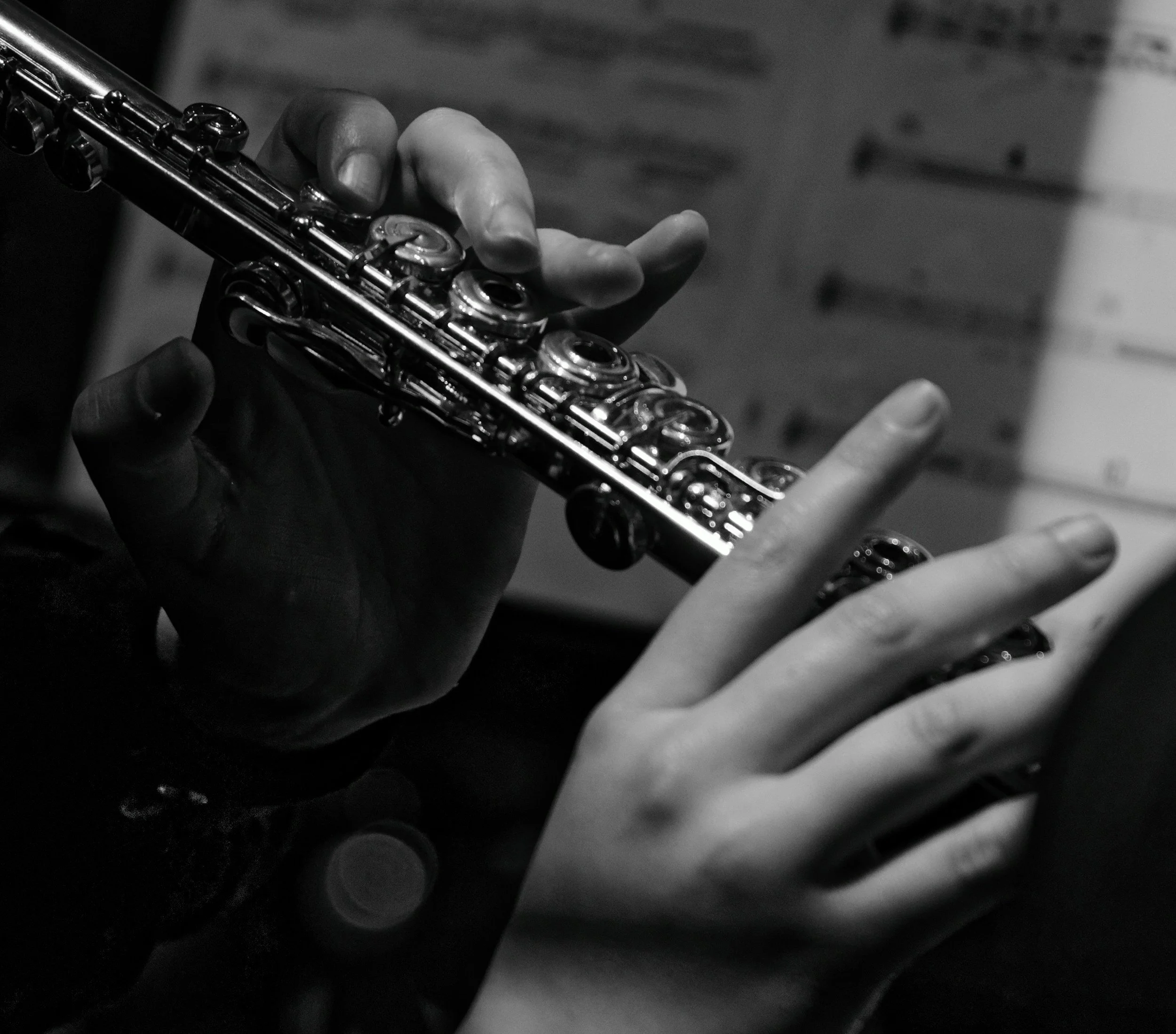 Close-up of a person playing a flute, hands holding and pressing the instrument's keys, black and white photo.