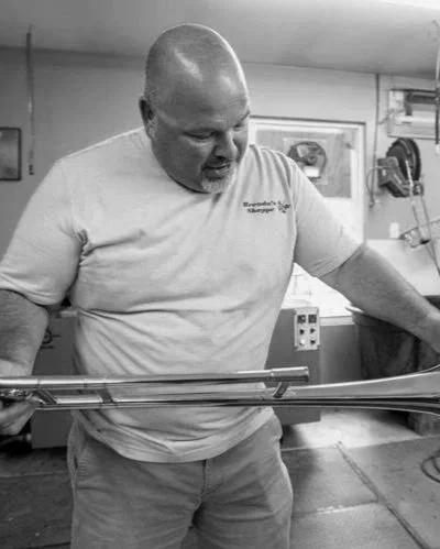 Man with a shaved head looking down at a metal object on a table in a workshop or kitchen.