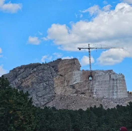 A construction crane on top of a rocky hill or mountain with blue sky and clouds in the background.