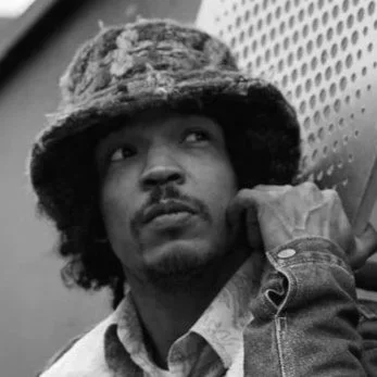 Portrait en noir et blanc d'un homme portant un chapeau en fourrure et une veste, regardant légèrement vers la gauche.