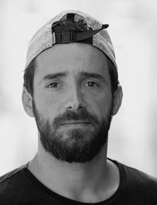 Un homme avec une barbe, portant une casquette à l'envers, visage sérieux, noir et blanc.