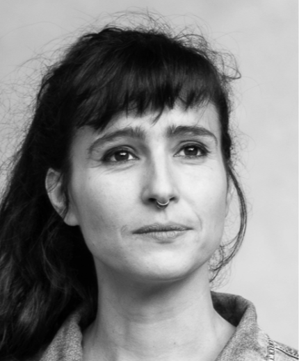 Portrait en noir et blanc d'une femme avec des cheveux foncés, un piercing au septum, et portant une veste