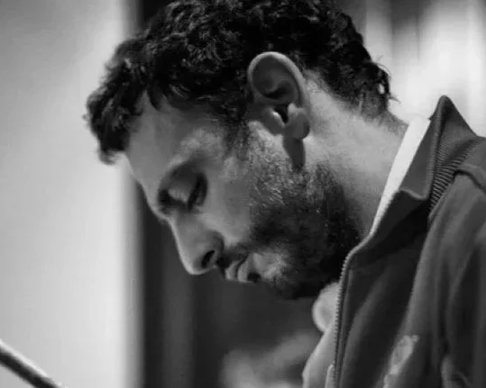 Un homme avec des cheveux bouclés et une barbe, vu en profil, dans une photo en noir et blanc.