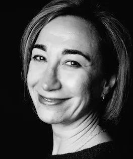 Portrait en noir et blanc d'une femme souriante avec des cheveux courts, portant une tenue sombre.