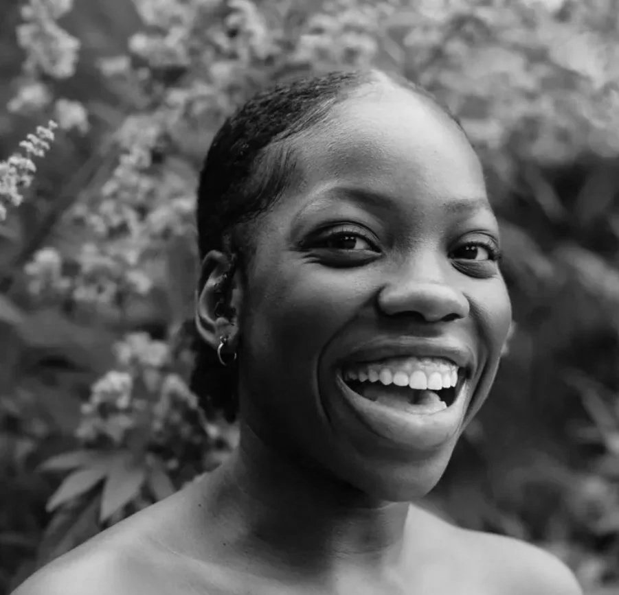 Une femme souriante avec court cheveux, en noir et blanc, en extérieur avec des fleurs en arrière-plan.