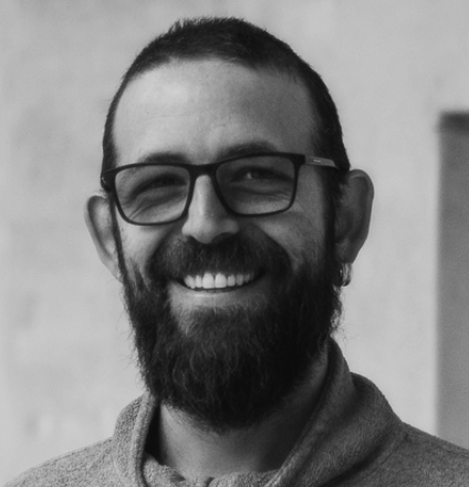 Portrait d'un homme avec des lunettes, une barbe et un sourire, en noir et blanc.