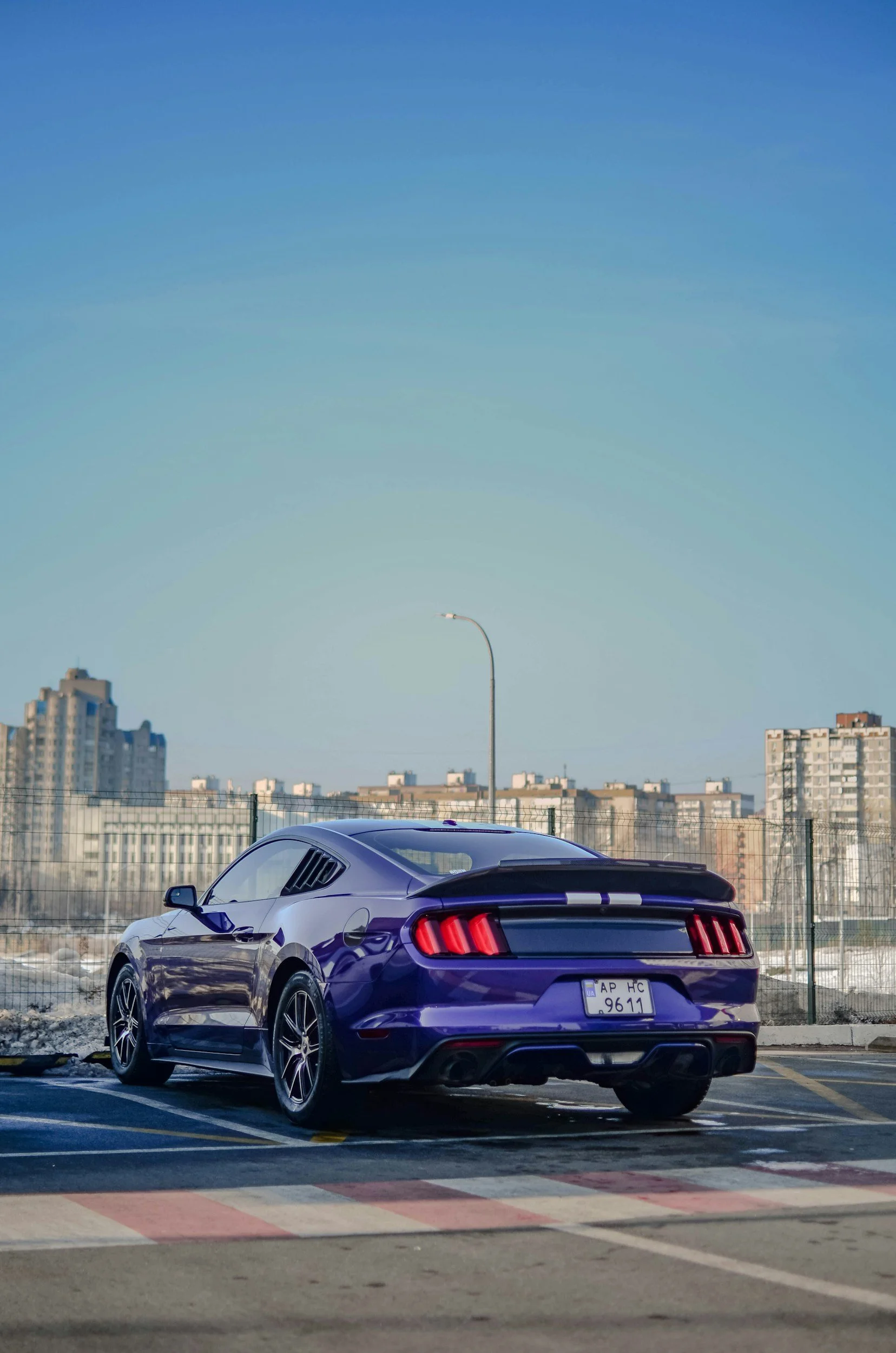 A purple sports car parked in a lot with a city skyline and a clear blue sky in the background.