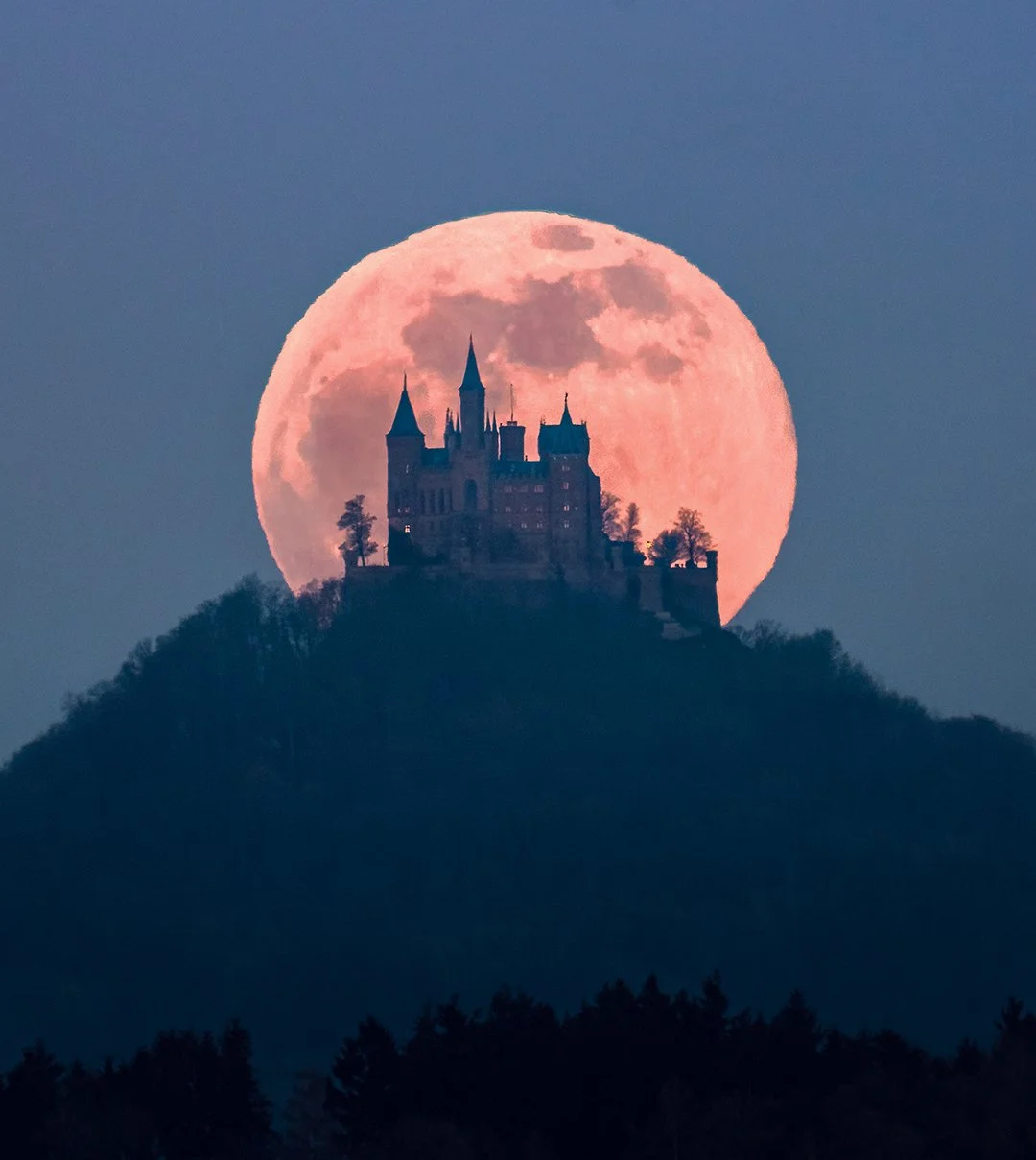 Schloss auf einem Hügel vor einer großen, rosa Vollmondnacht.