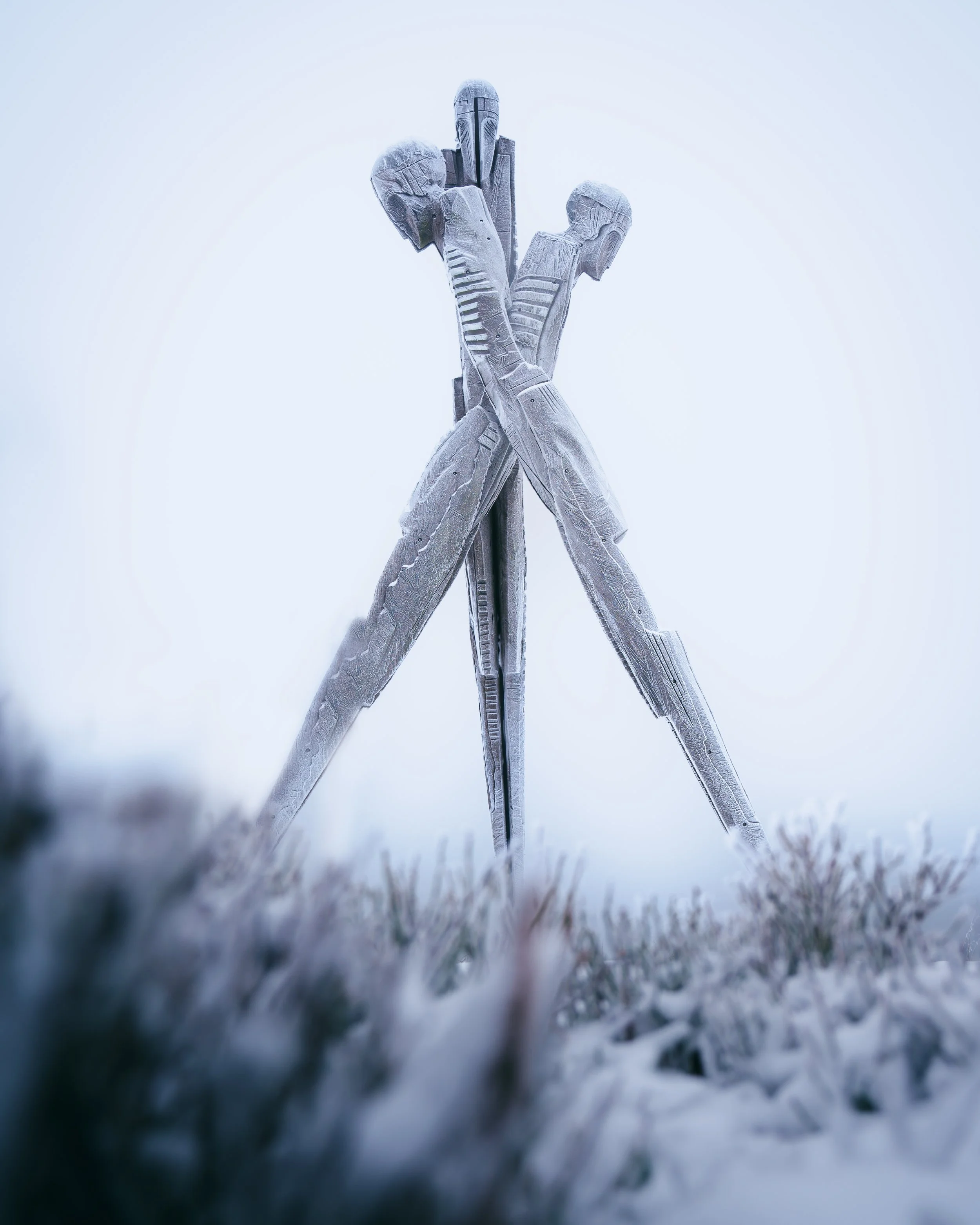 Kunstwerk einer Skulptur, die eine in mehrere Richtungen auseinandergehende menschliche Figur zeigt, aus Metall gefertigt, im winterlichen Schnee aufgestellt.