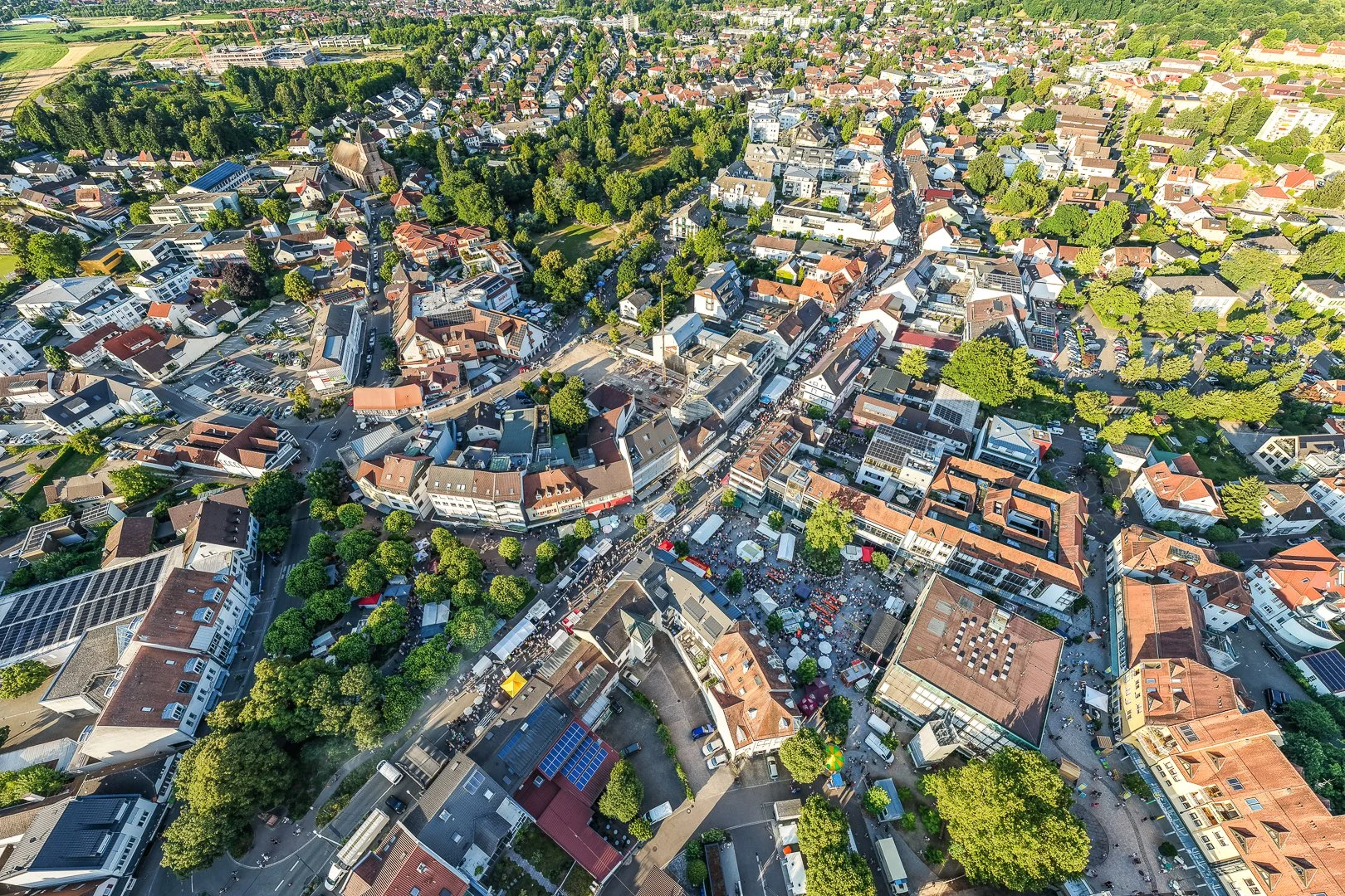 Luftaufnahme einer Stadt mit vielen Gebäuden, Straßen und grünen Parks, bei Sonnenlicht