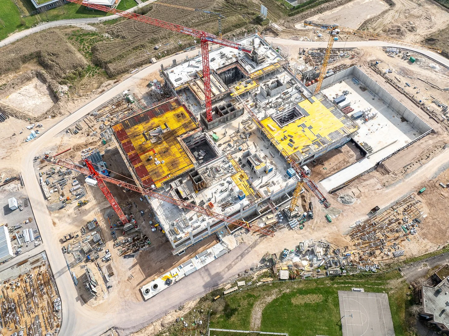 Luftaufnahme eines Baustellenbereichs mit mehreren Baukränen, Gebäudefundamenten und Baumaterialien