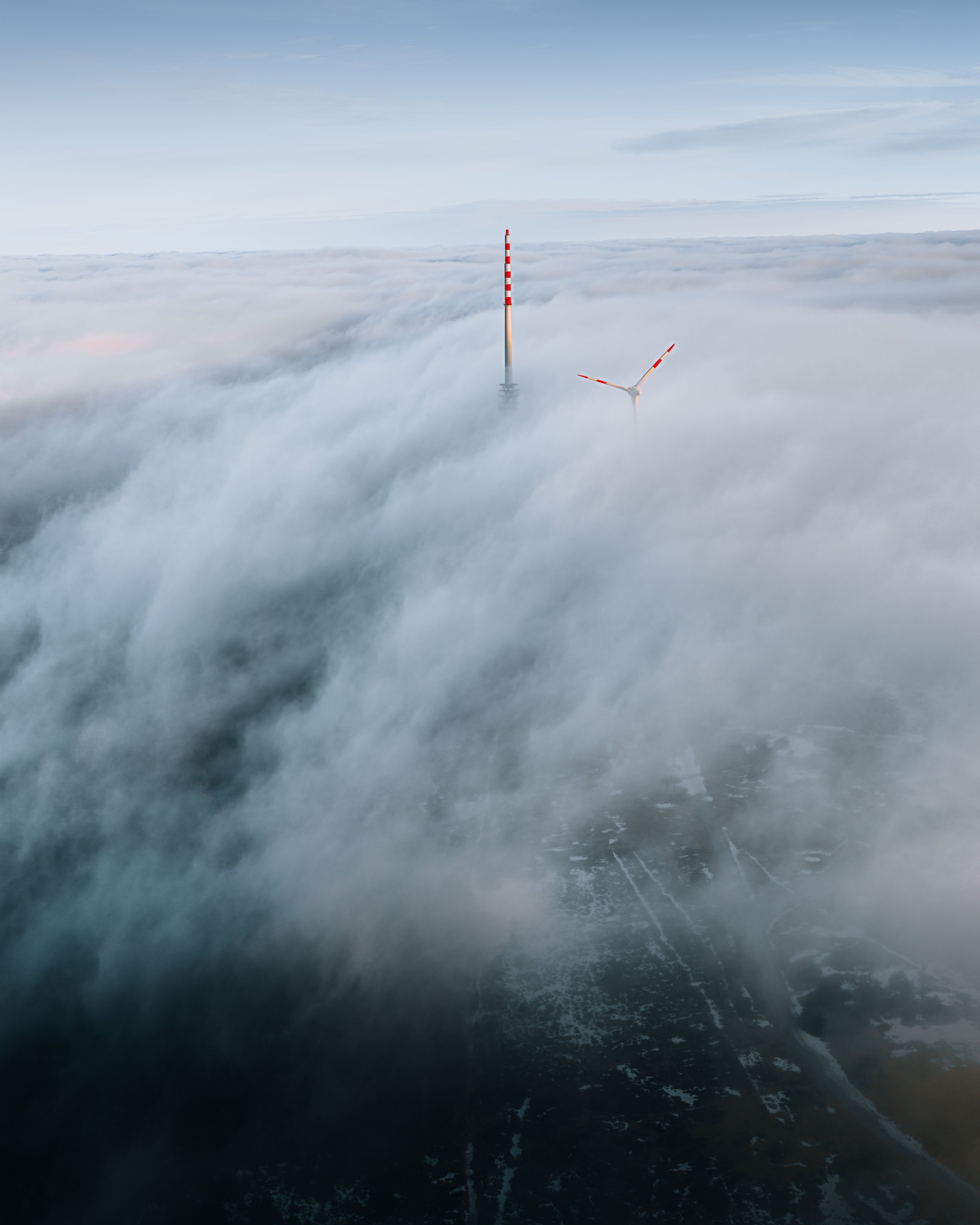 Windkraftanlage und Beobachtungsturm in Wolken gehüllt, mit Wasser im Vordergrund.