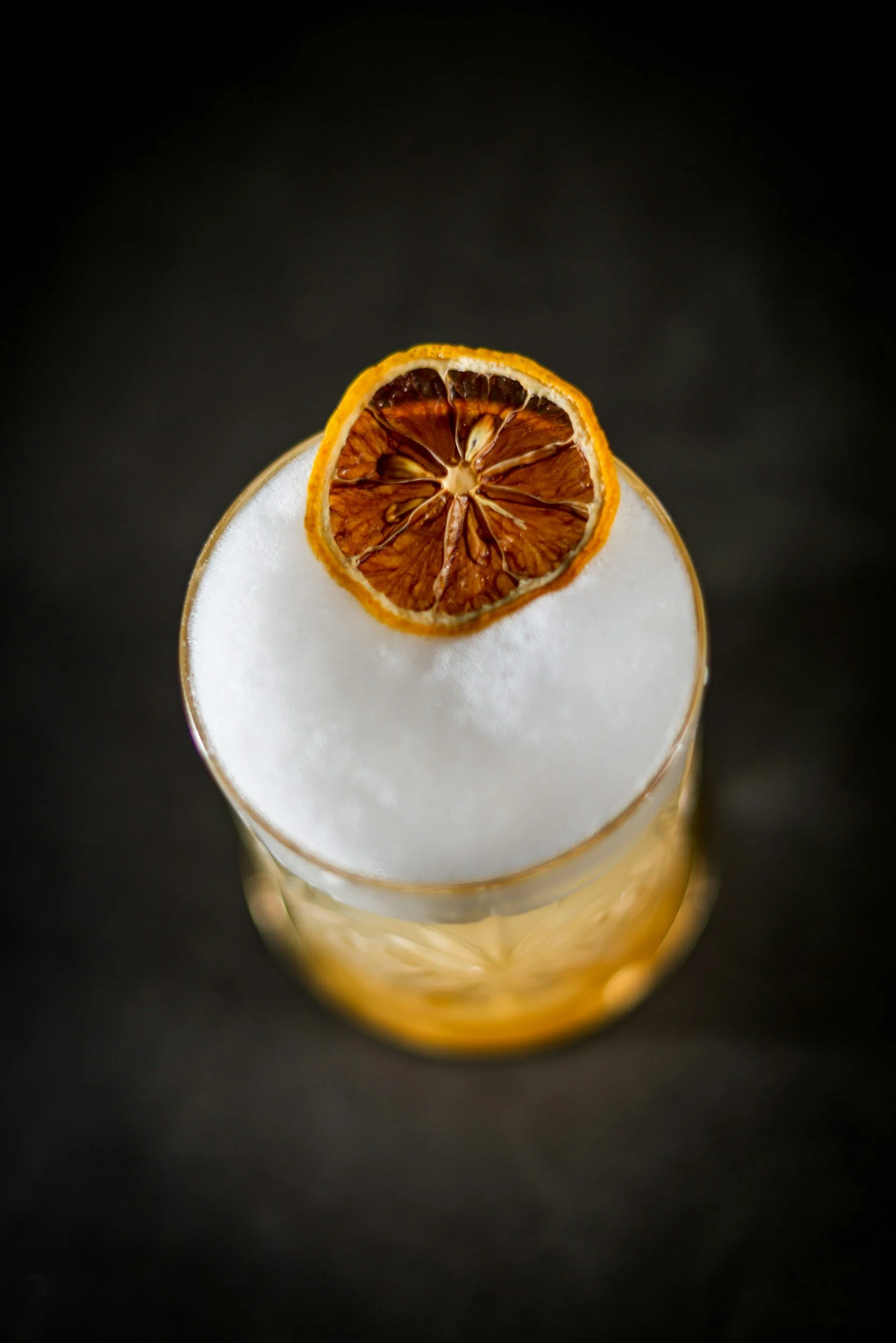 A glass drink topped with frothy foam and garnished with a dried orange slice.