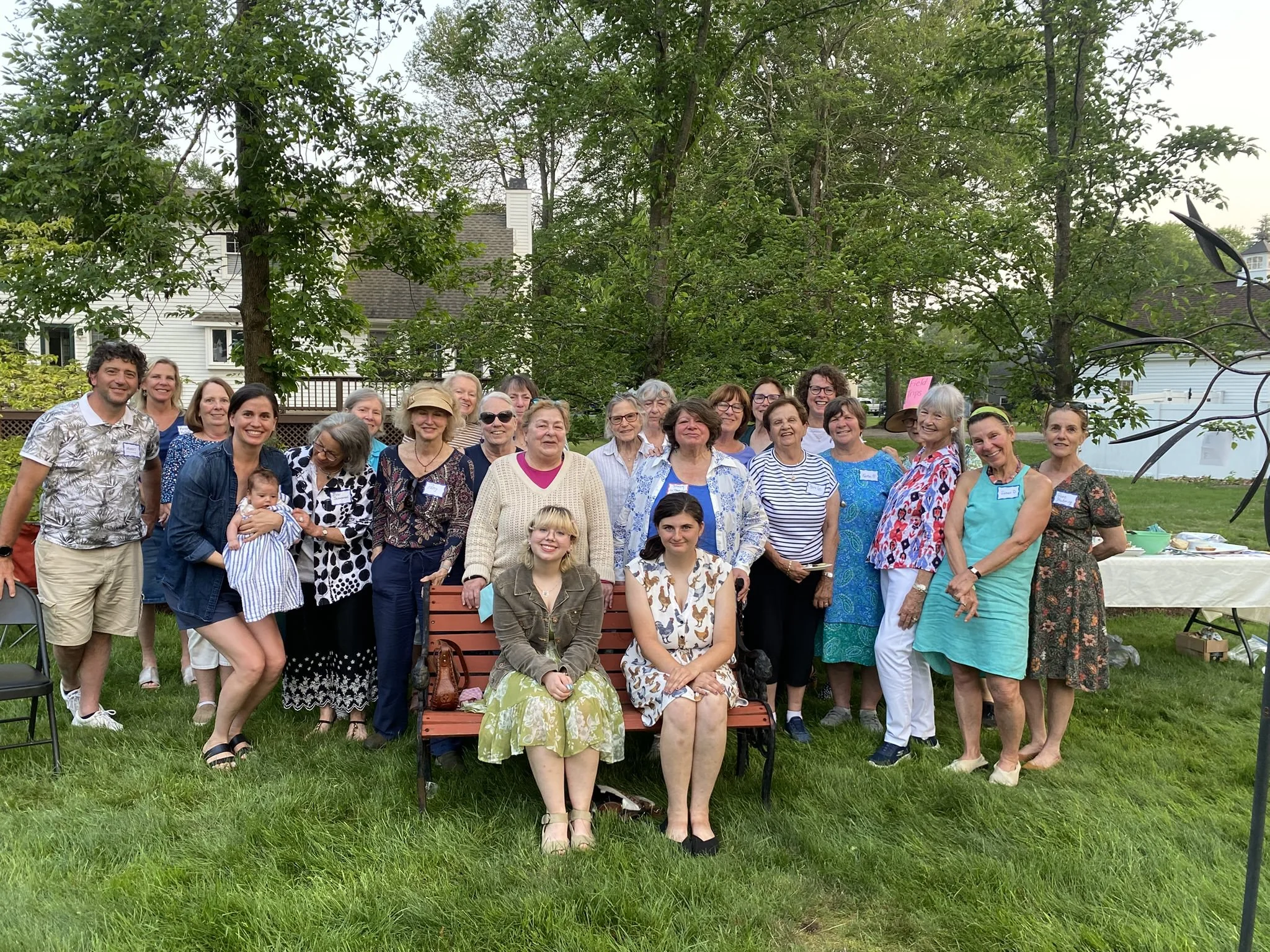 Group of adults and children posing outdoors during a gathering or event, with trees and houses in the background.