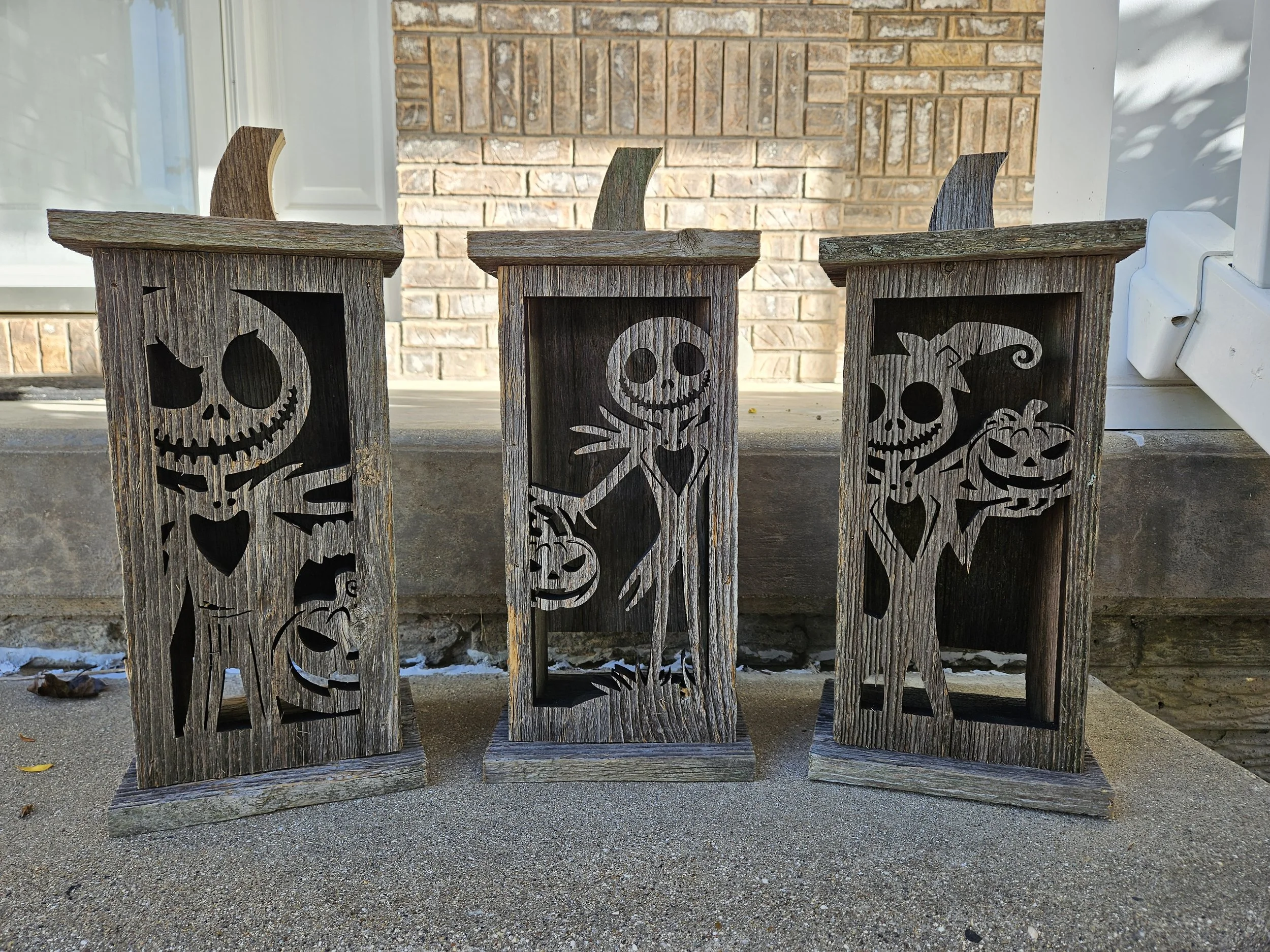 Three rustic wooden jack o' lanterns with Halloween-themed cutouts depicting a skeleton, a smiling skull, and a smiling pumpkin