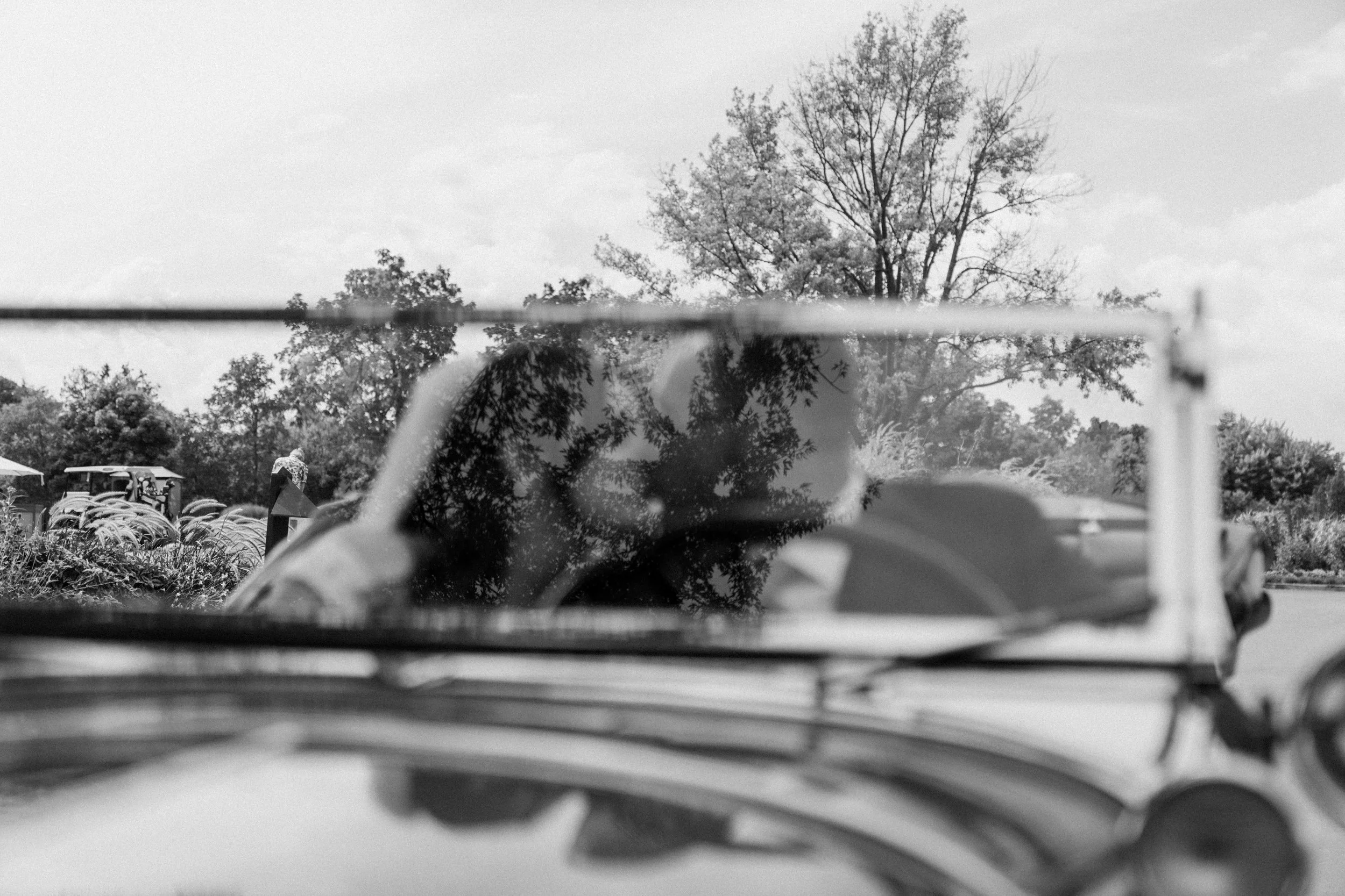 Black and white photo showing the reflection of a married couple in a vintage car  on their Wedding day 