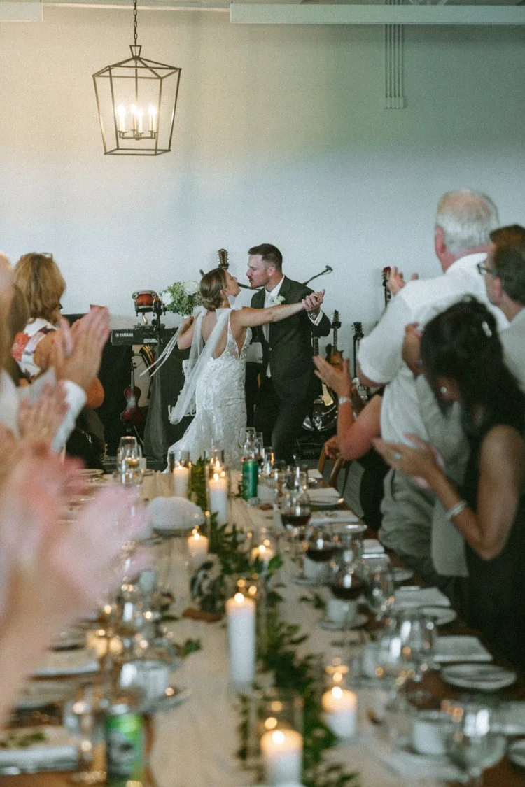 A bride and groom dancing at their wedding reception surrounded by seated guests clapping and celebrating.