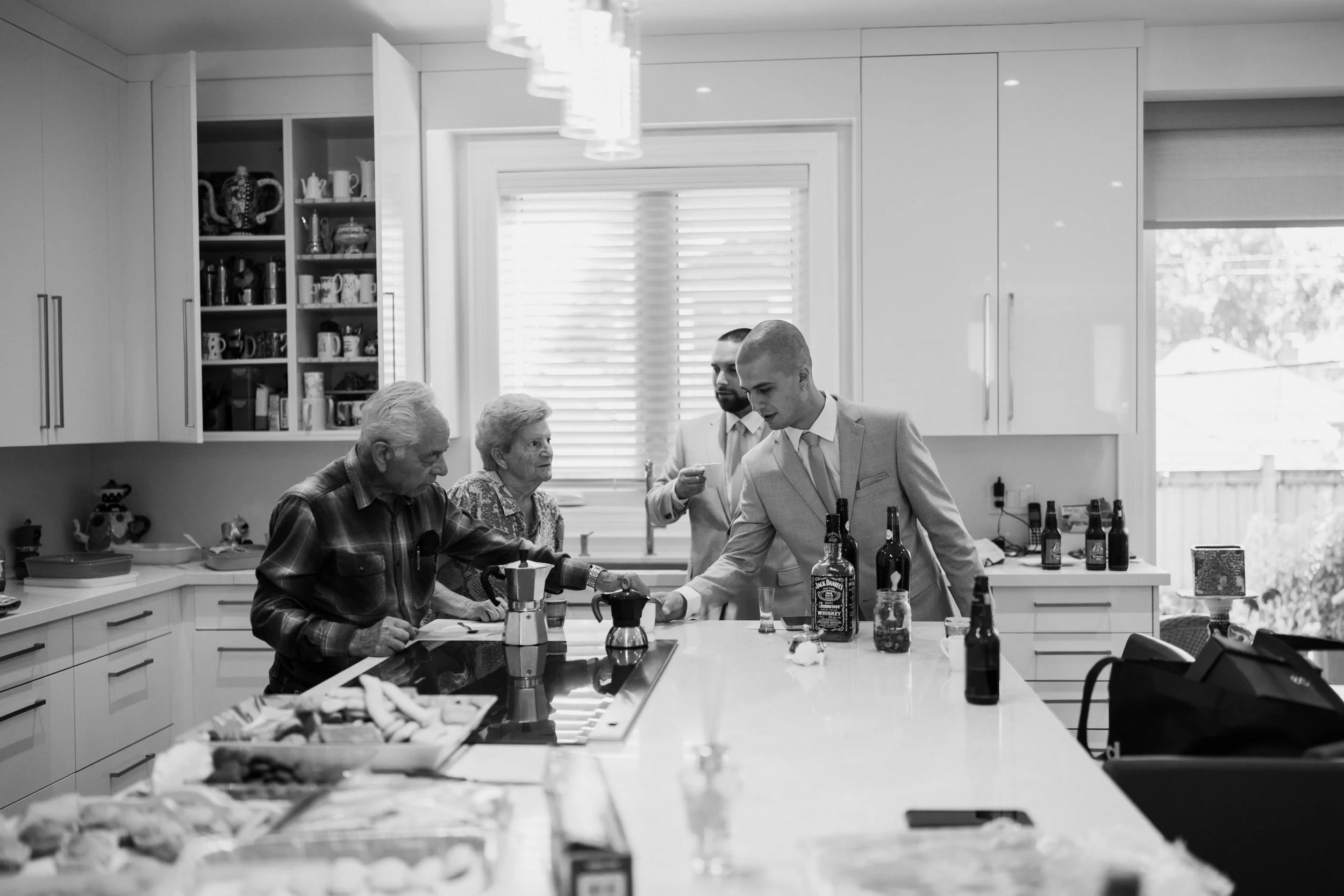 People gather in a modern kitchen, serving drinks and socializing, with food on the counter.