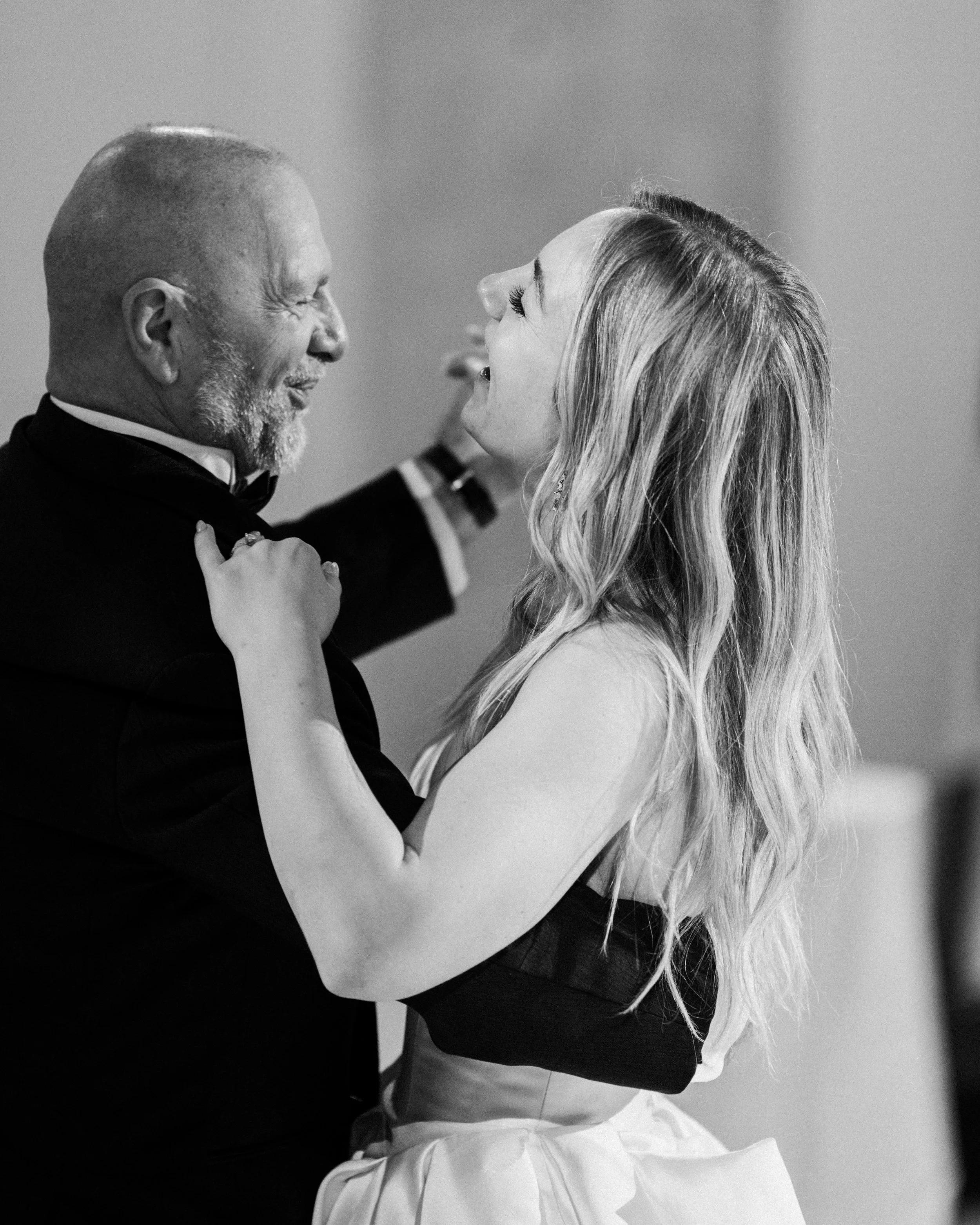 A black and white photo of an elderly man and a young woman dancing happily, holding each other closely and smiling.