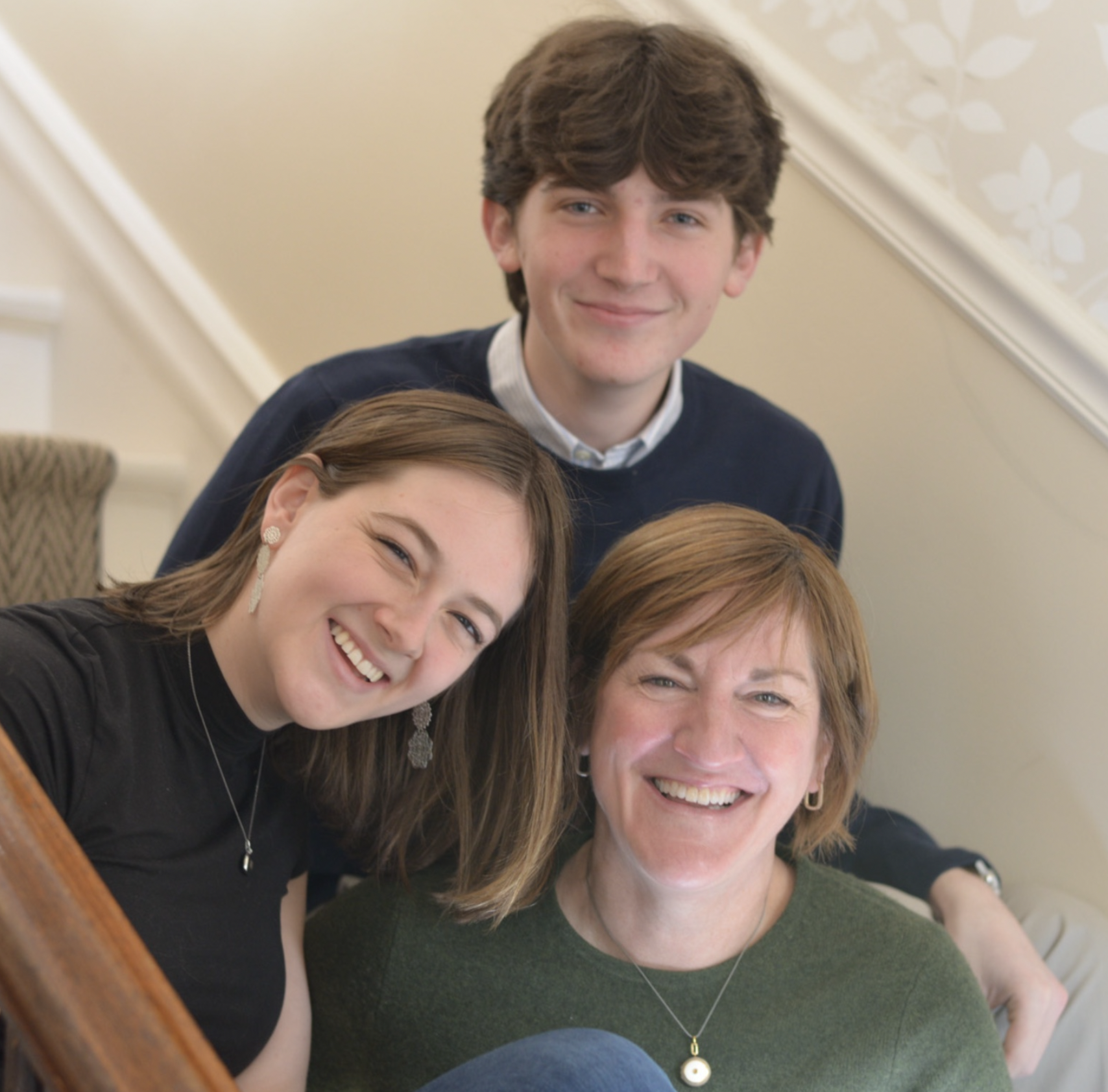 A family of four smiling together on stairs in a home setting.