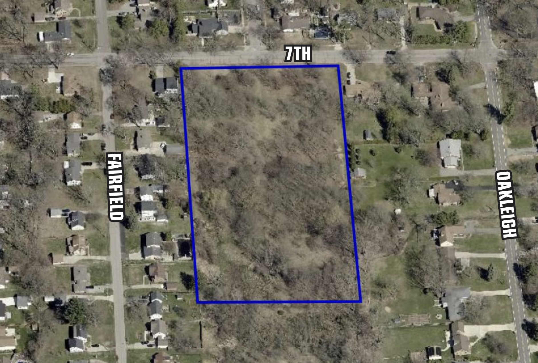 An aerial view of a residential neighborhood showing a large empty wooded lot outlined in blue, bordered by Fairfield Avenue on the left, 7th Street at the top, and Oakleigh Avenue on the right.