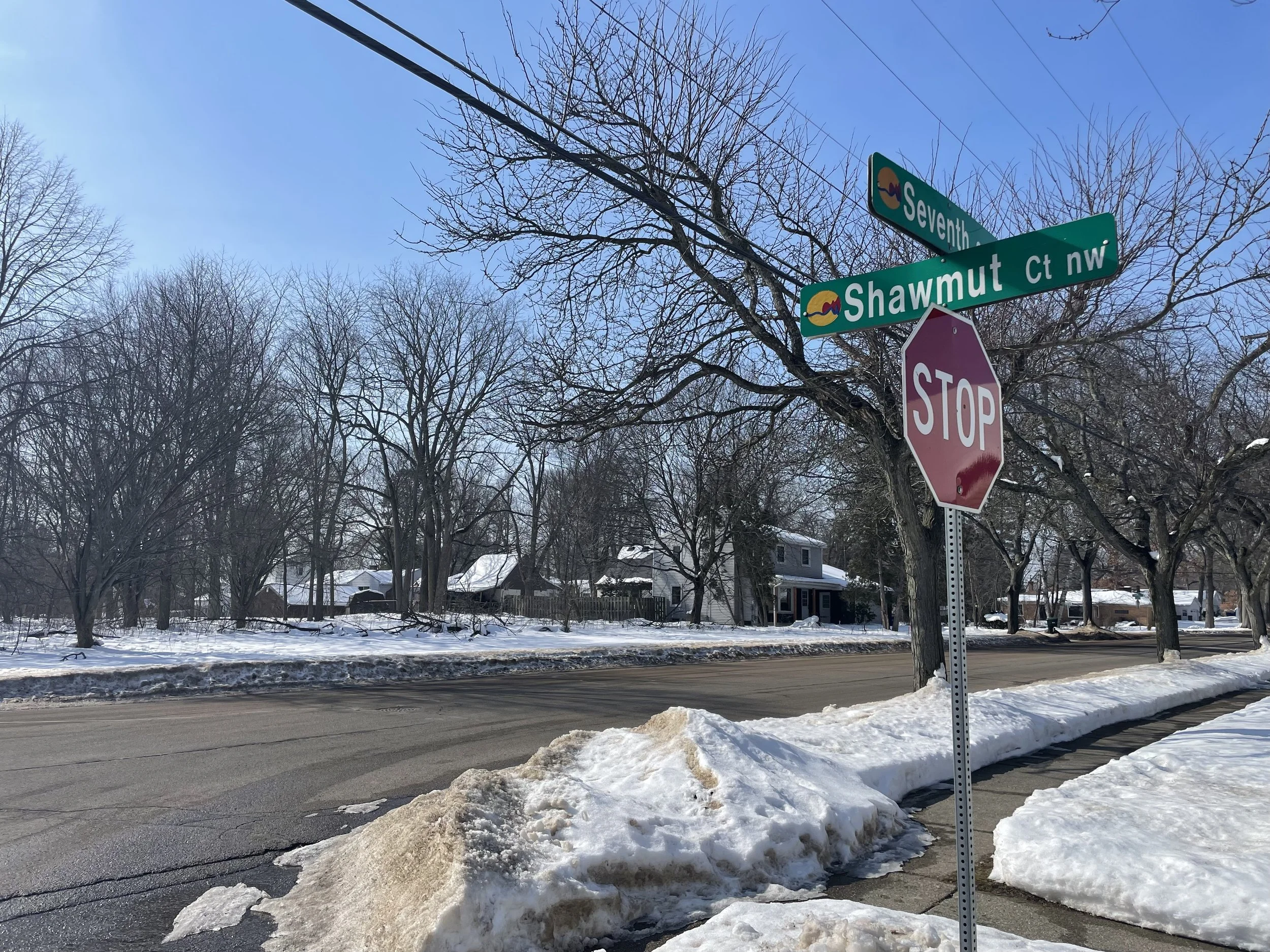 Street corner in Shawmut Hills on Grand Rapids' West Side. Street signs indicate Seventh and Shawmut streets. Houses and leafless trees are in the background, and the sky is clear and blue.