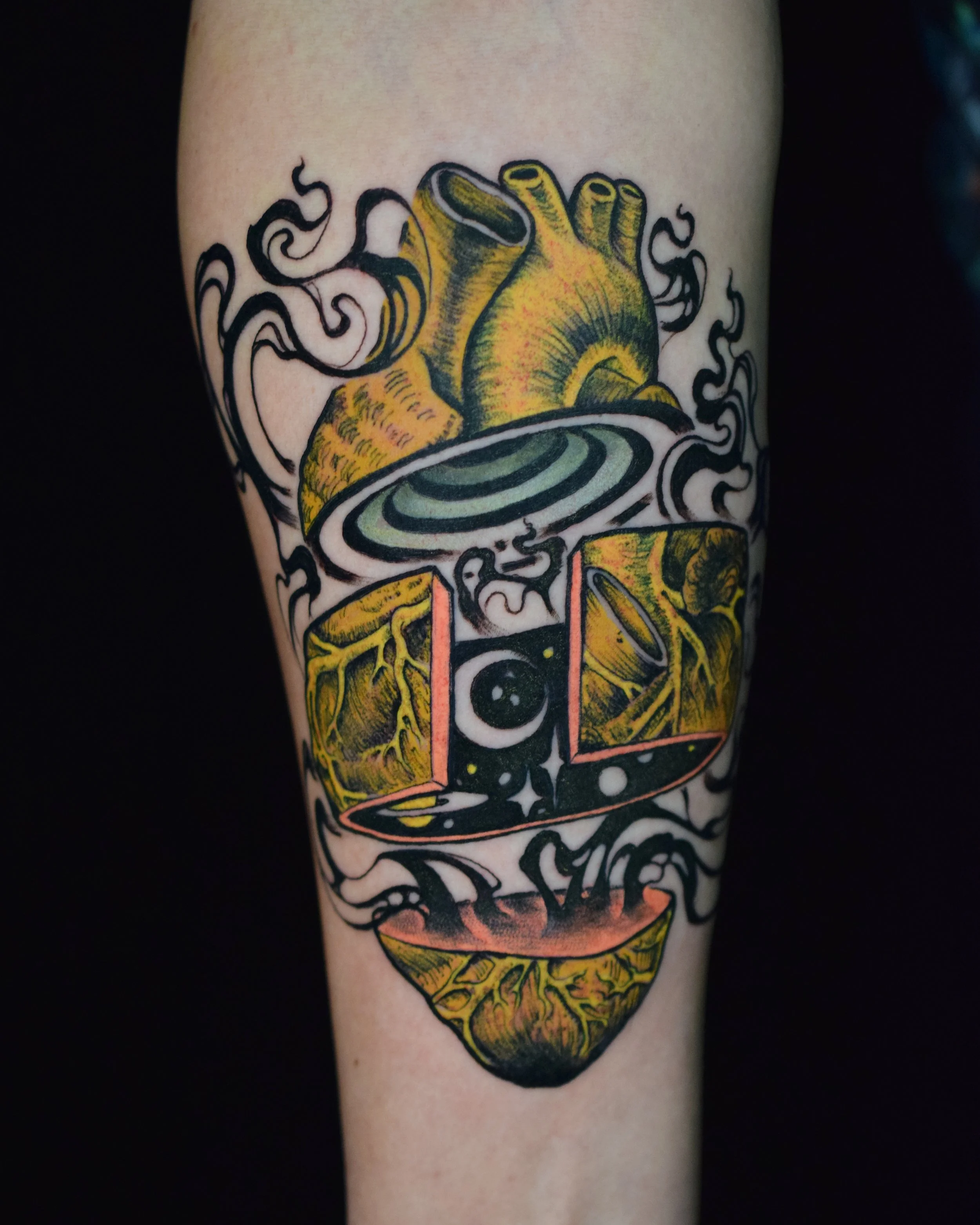 Colorful tattoo of a human heart with swirling smoke, a cosmic eye, and abstract geometric shapes on a person's arm.