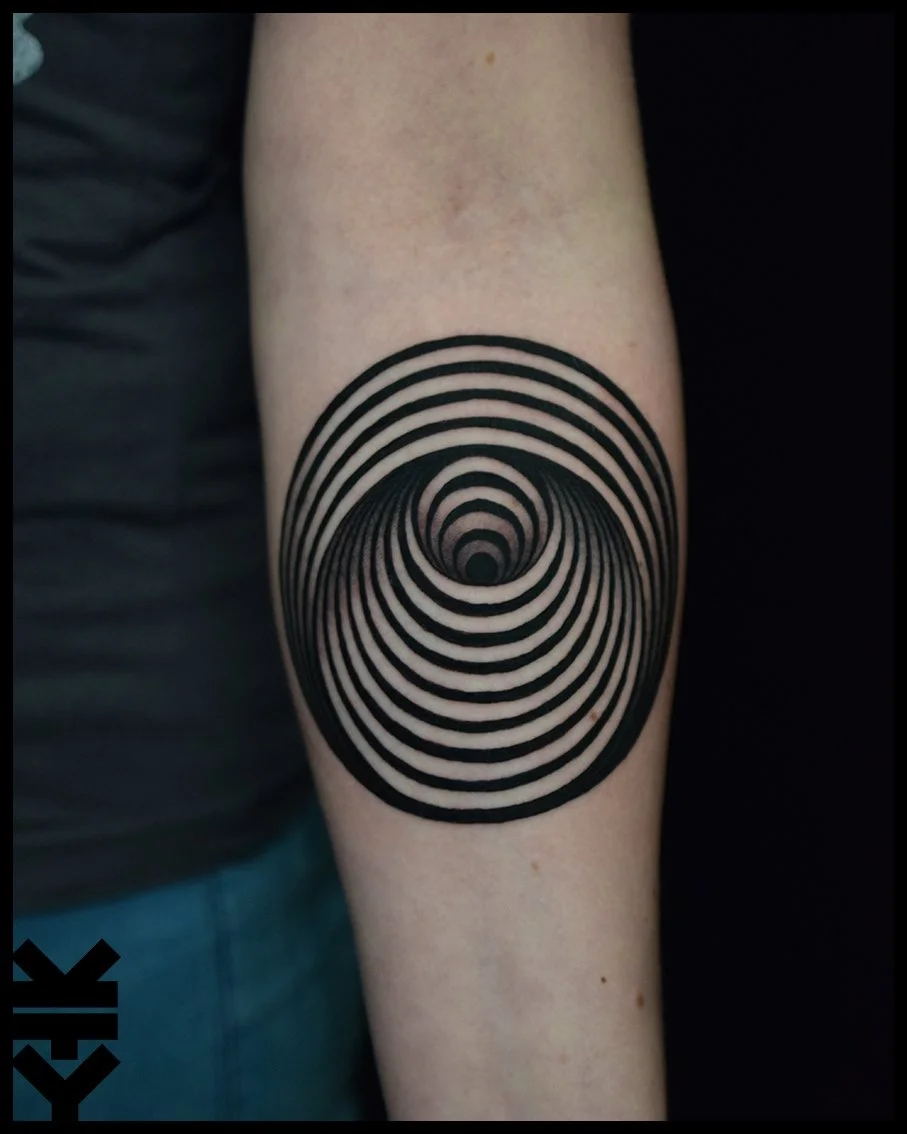 Tattoo of concentric black circles creating an optical illusion on a person's upper arm.